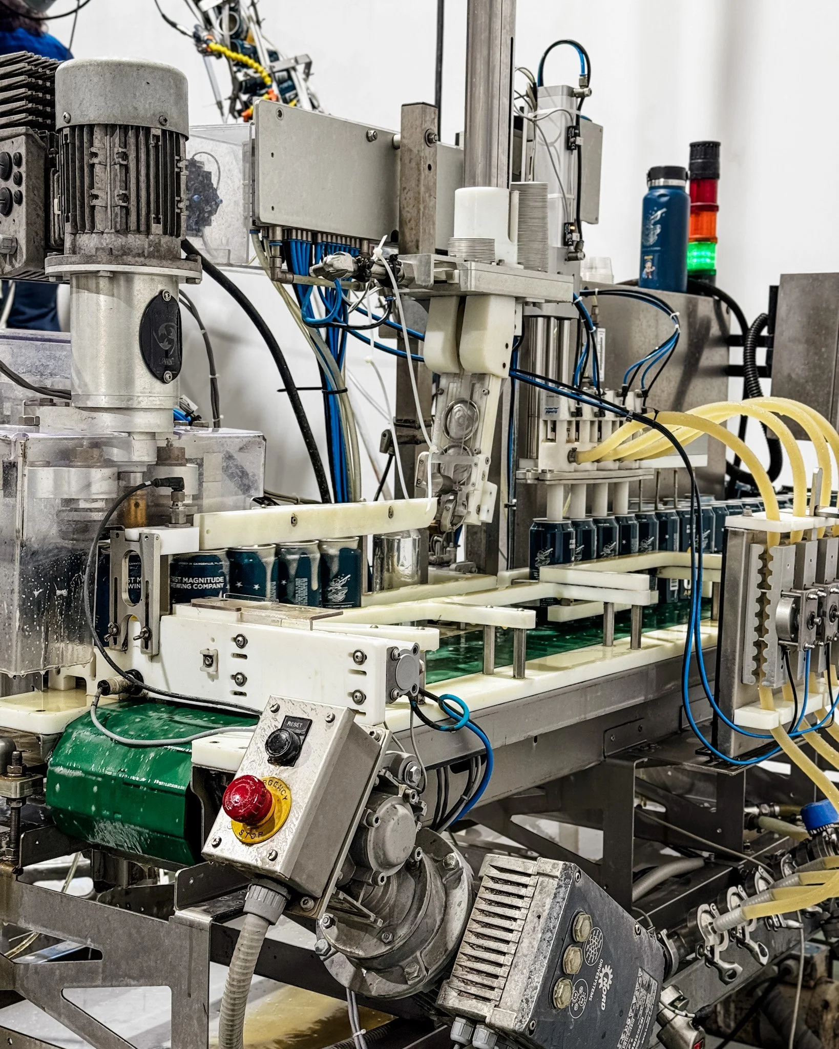 Close-up view of complex industrial machinery with multiple interconnected components, wires, and pipes, including electric motors, control panels, and fluid tubes.