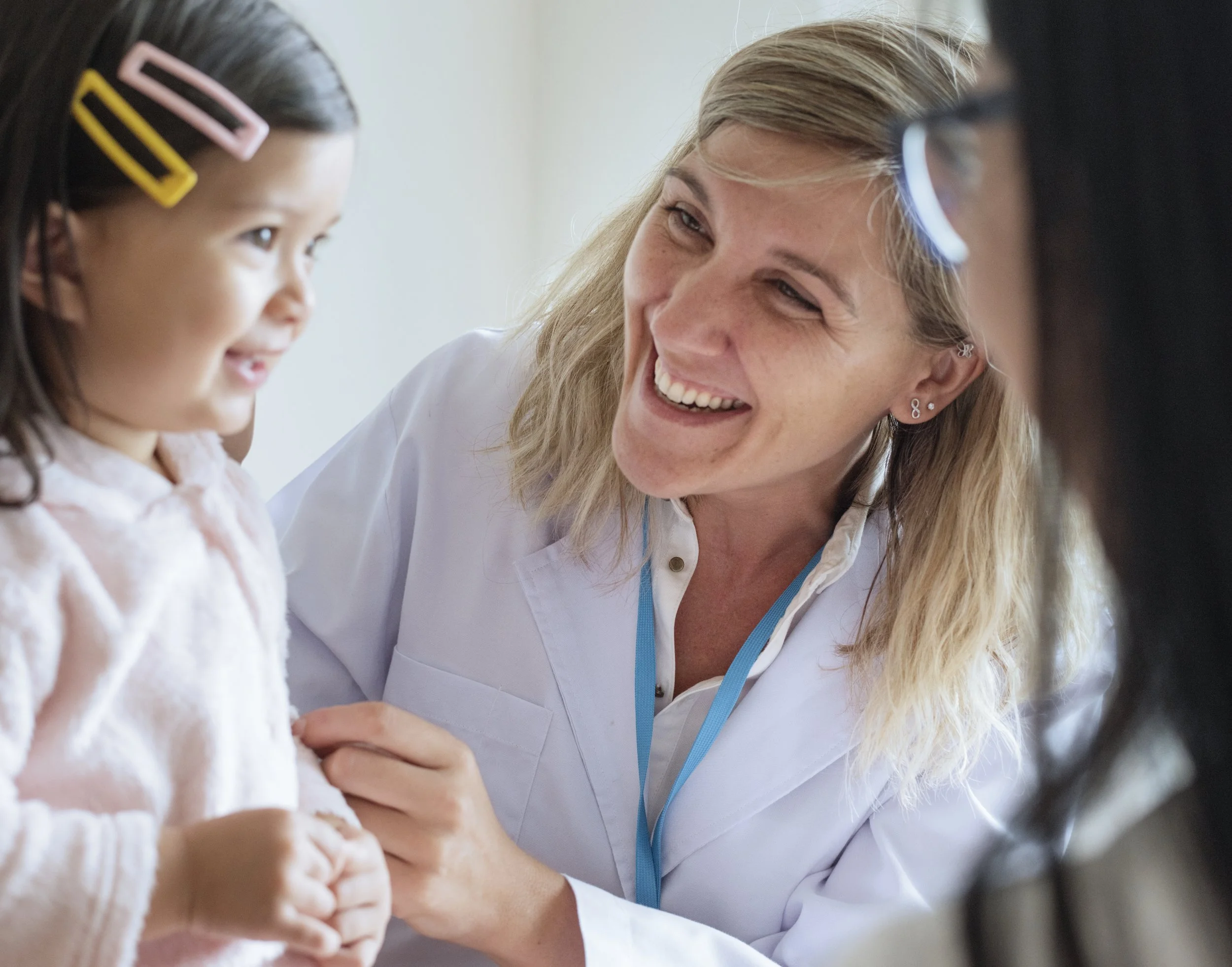A female nurse smiling and talking to a young girl with hair clips in her hair, both engaged in a conversation.