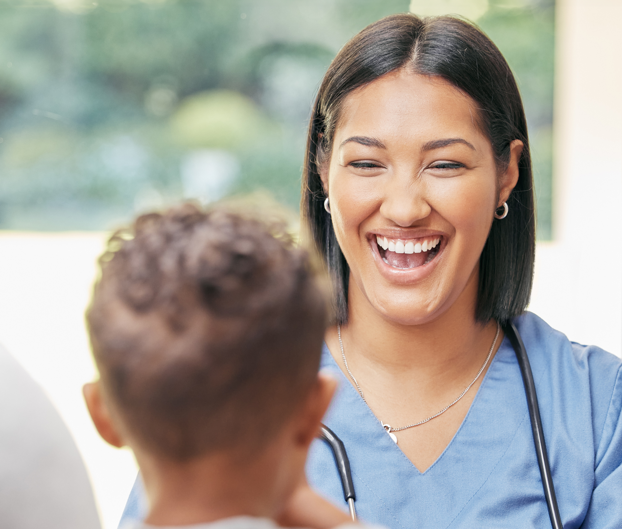 Close-up of a smiling woman wearing a blue medical uniform with a stethoscope around her neck, engaging with a patient.