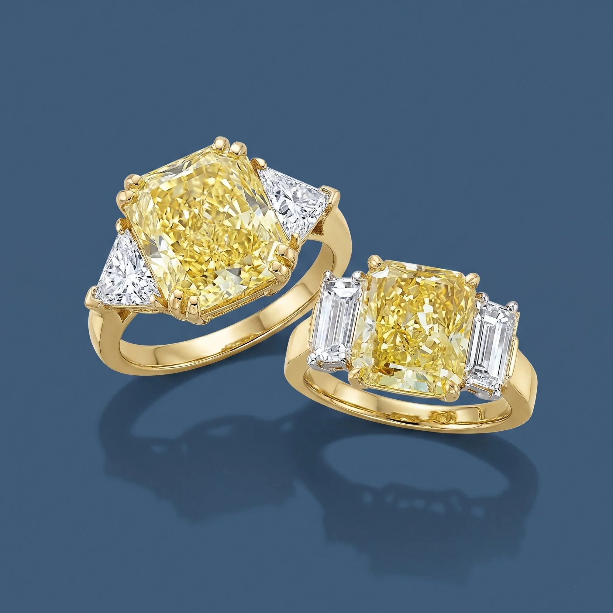 Two fancy intense yellow radiant cut diamond rings with trillion and emerald side stone accents in 18k yellow gold, part of the Coleman E. Adler III Private Collection in New Orleans