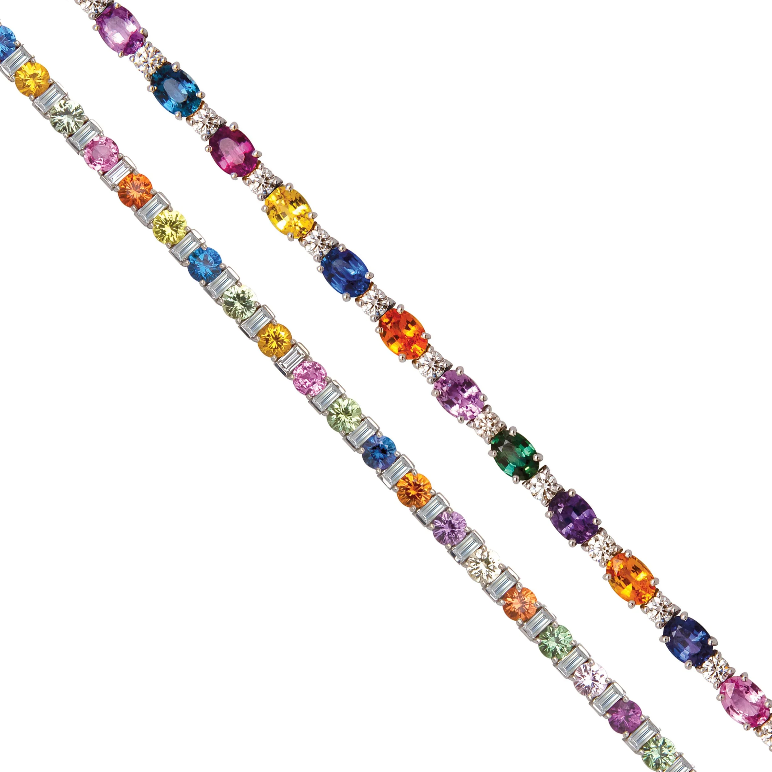 Close-up of two colorful gemstone and diamond bracelets with oval, round, and baguette cut stones in various colors.
