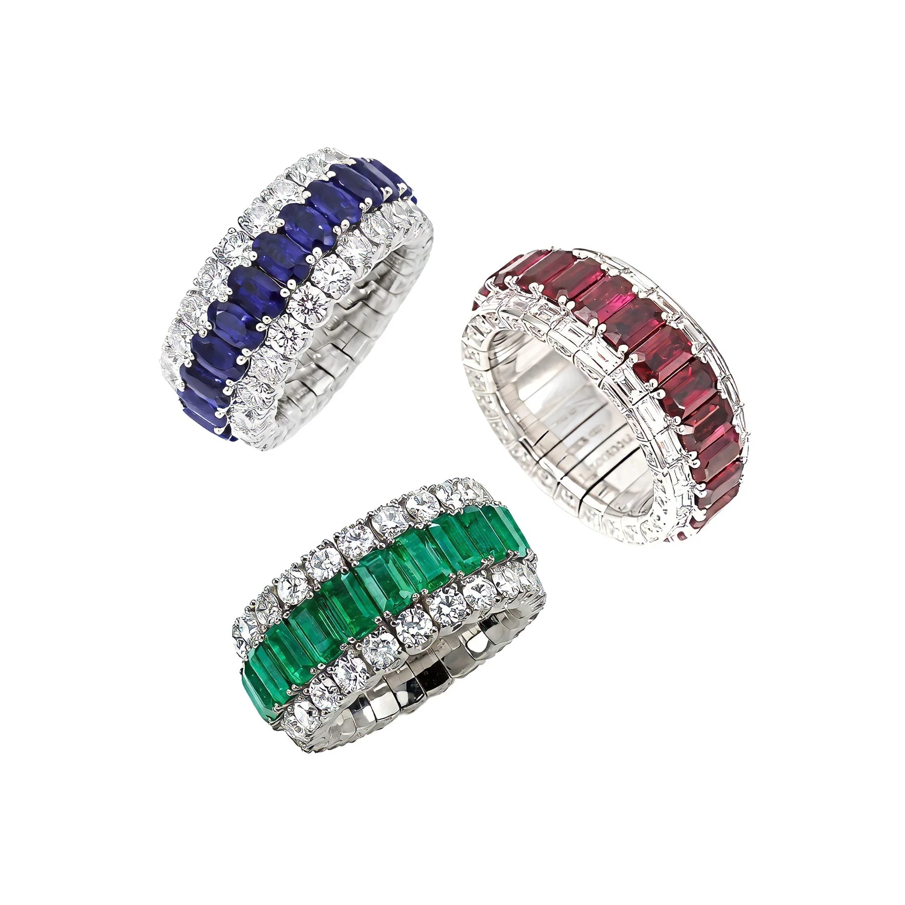 Three ornate rings each featuring striking gemstones: one with deep blue sapphires, one with rich red rubies, and one with vibrant green emeralds, all accented with sparkling diamonds set in silver or platinum bands.