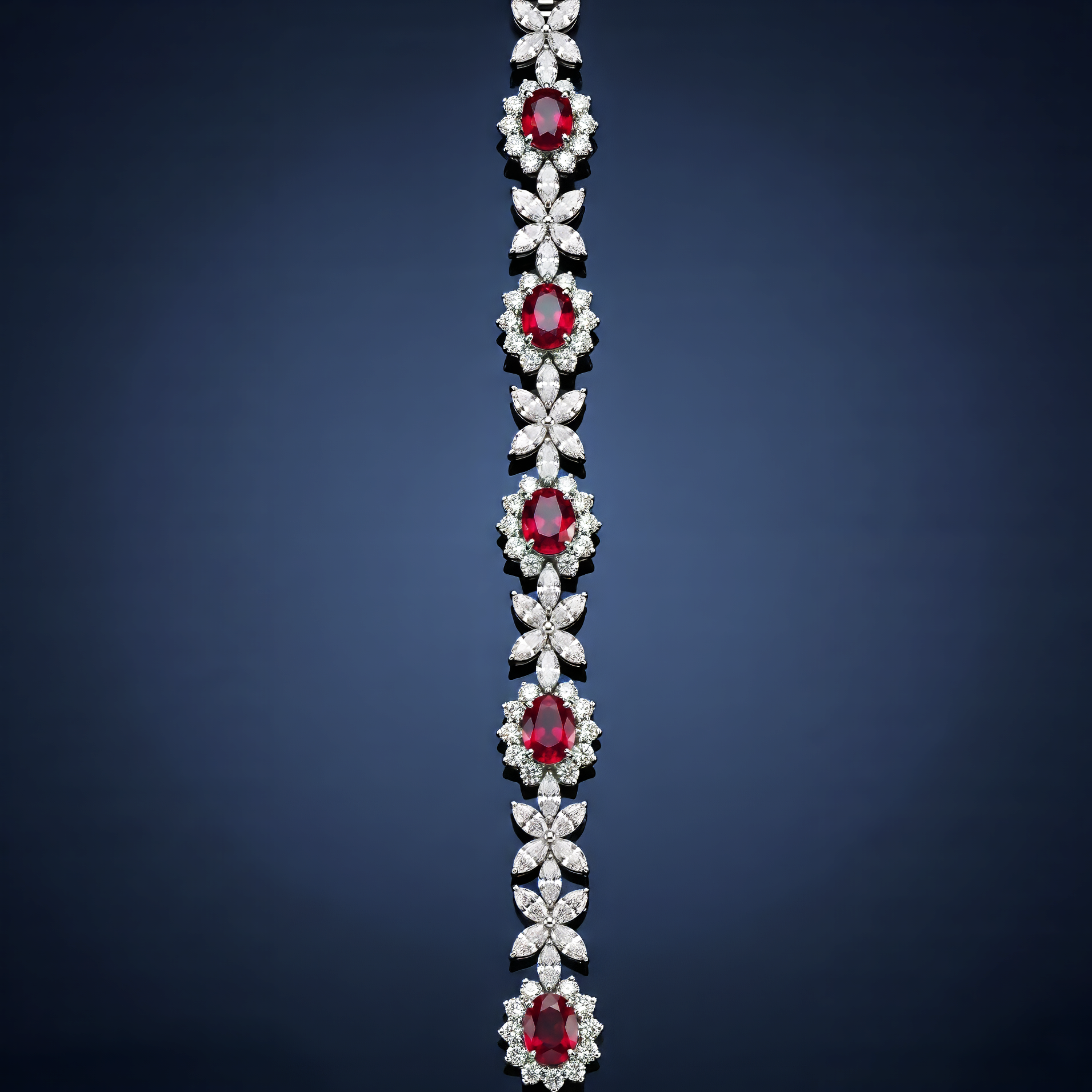 Close-up of a silver jewelry piece with multiple red gemstones and clear diamonds arranged in floral and leaf patterns, hanging against a dark background.