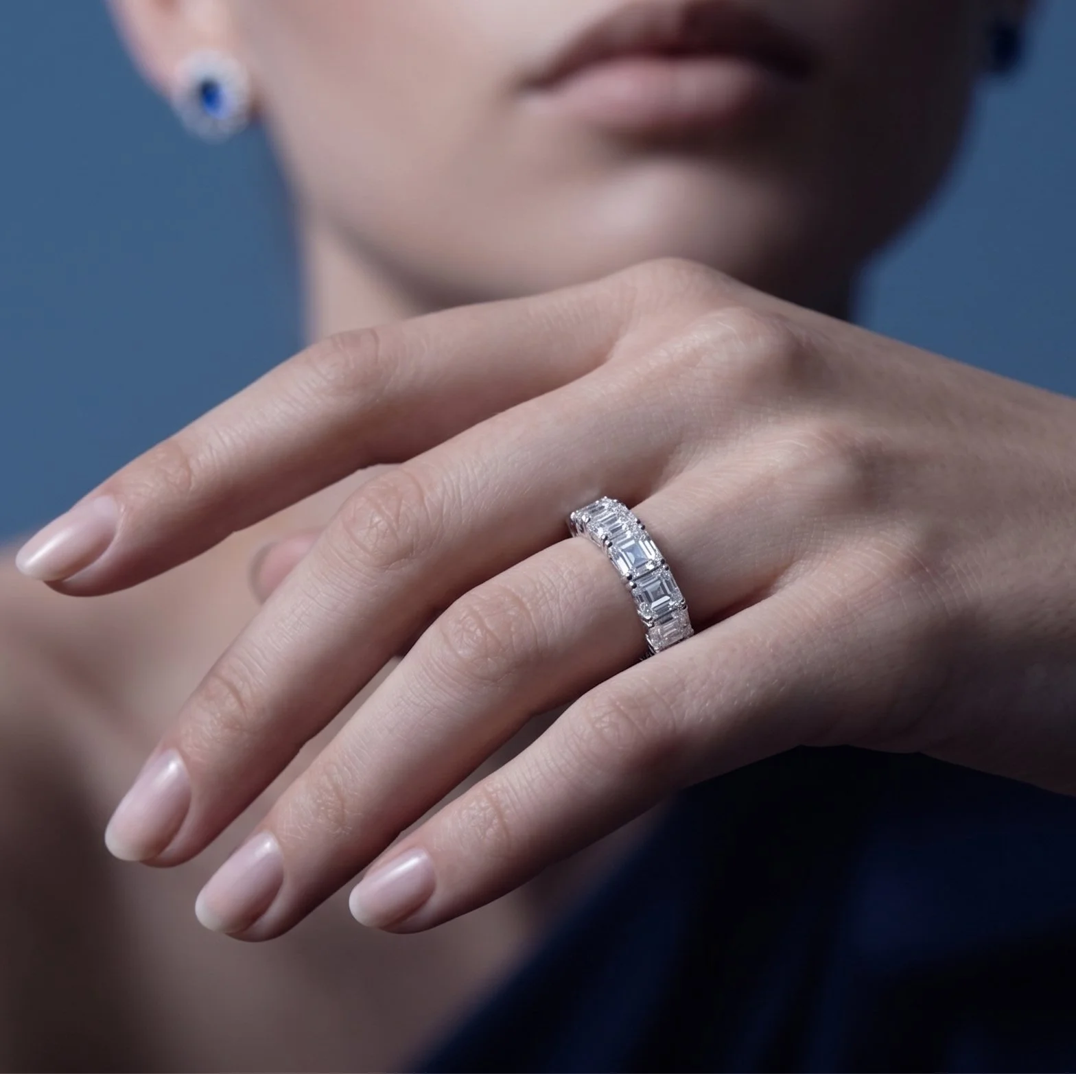 Close-up of a woman's hand wearing a sparkling diamond ring on her finger, with her lips and face slightly blurred in the background.