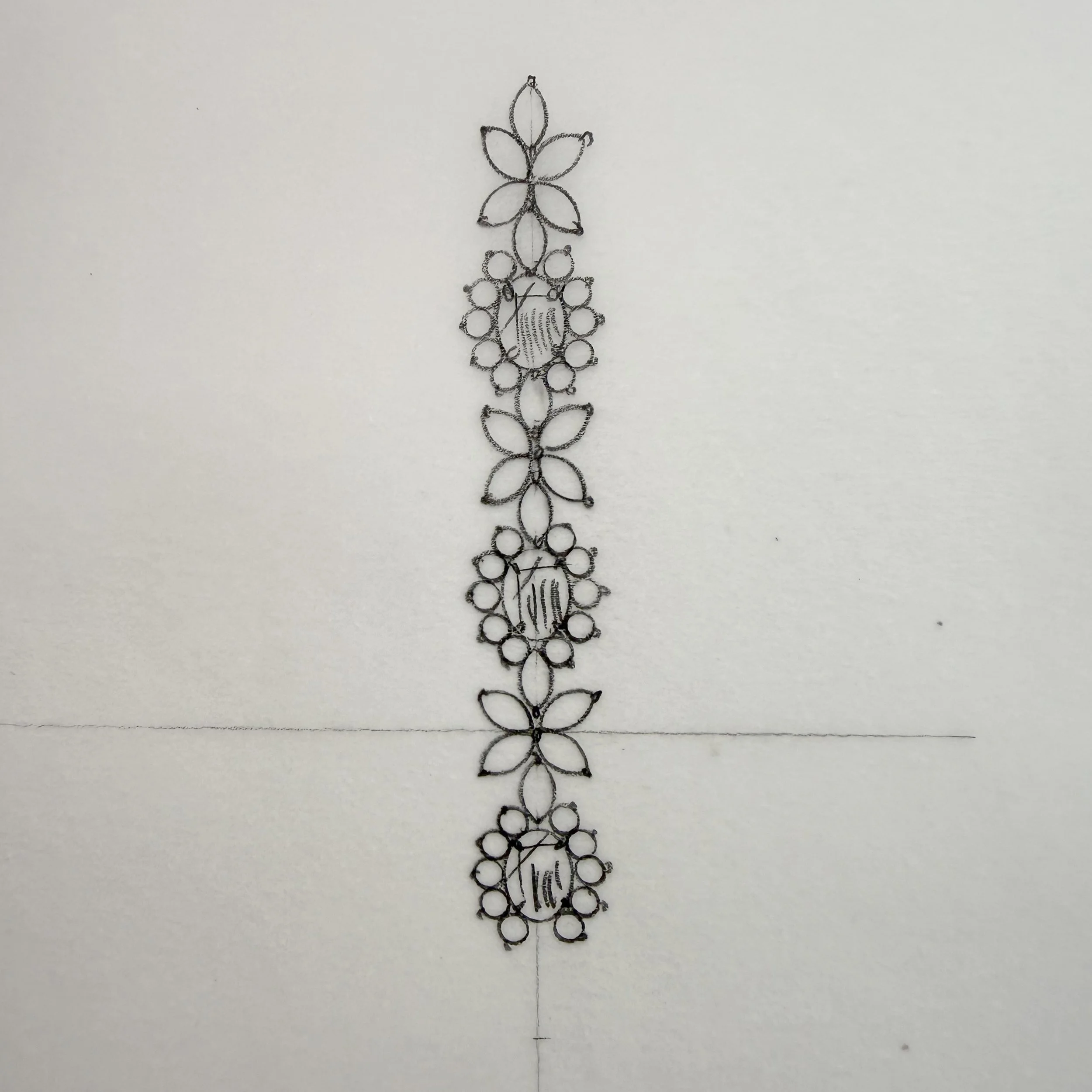 A vertically oriented silver necklace with multiple small loops forming flower and leaf shapes, arranged in a symmetrical pattern.