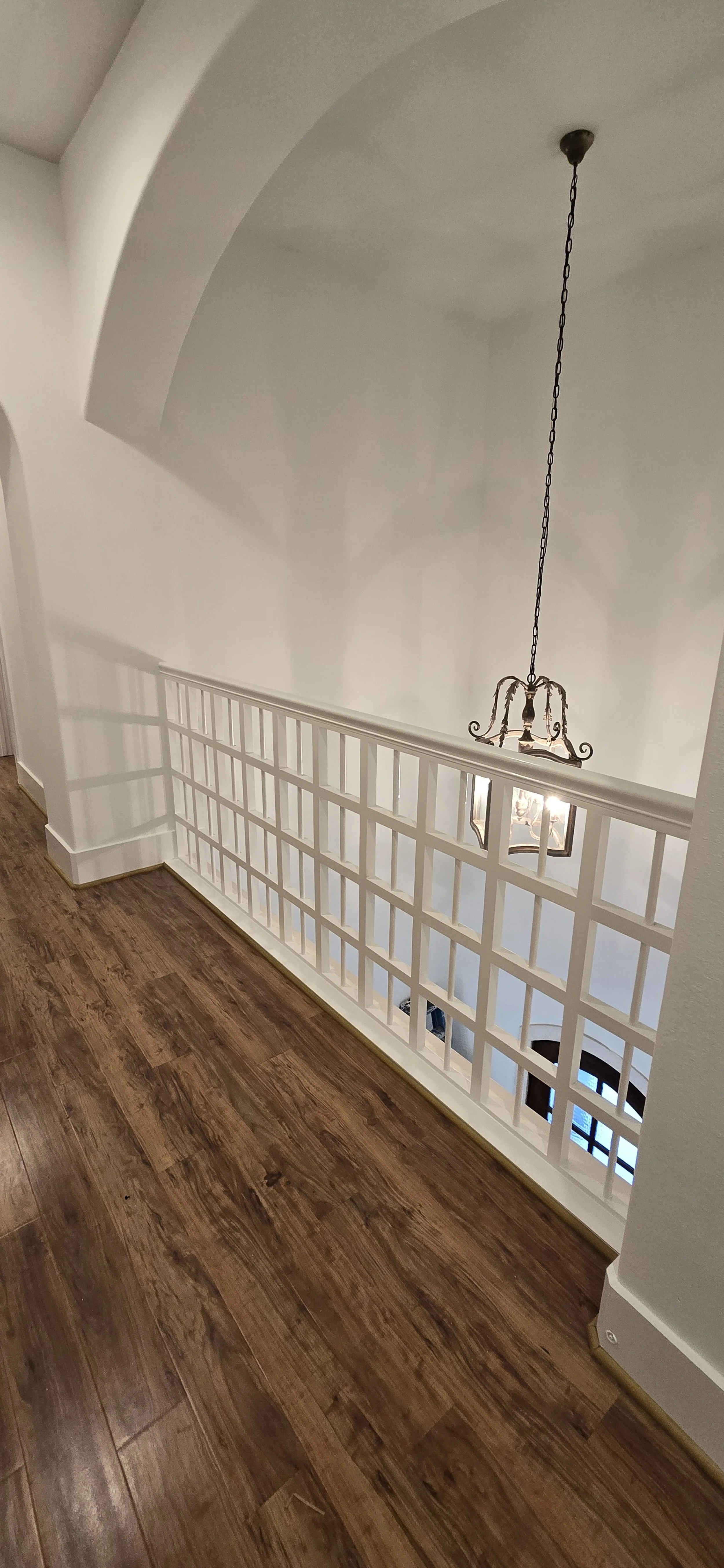 View of an indoor staircase with a decorative hanging chandelier, white walls, and dark wood flooring.