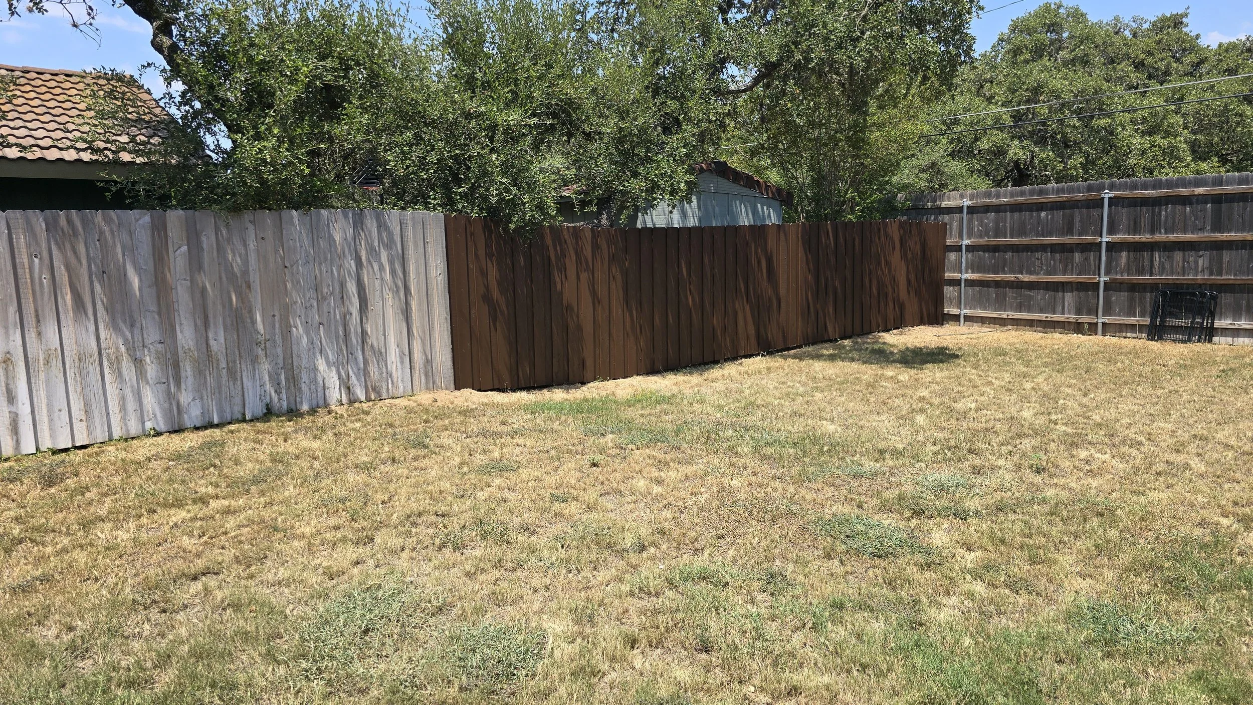Backyard with multi-colored wooden fence, some trees, and a grassy lawn