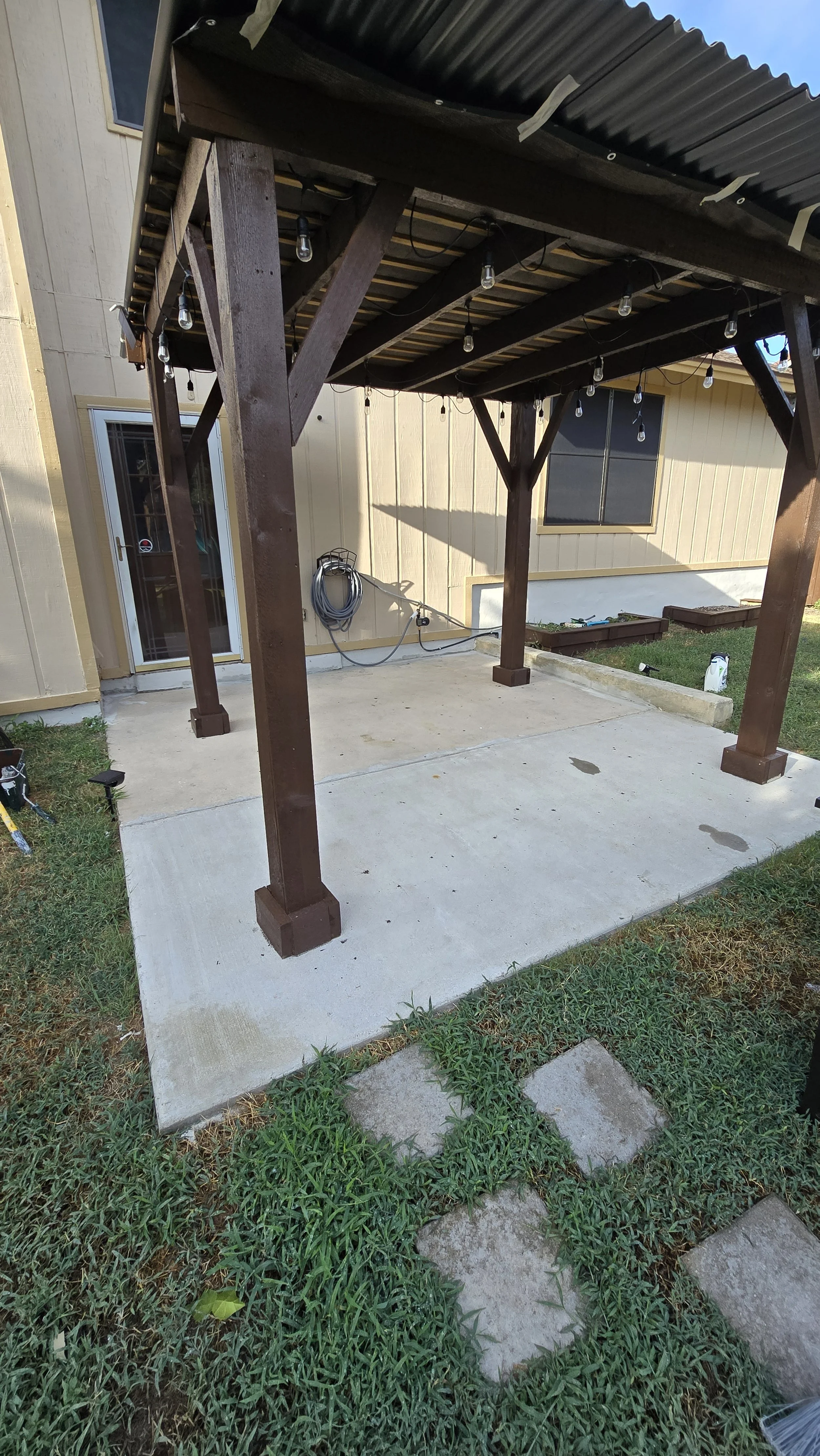 A newly built wooden porch with a concrete slab, string lights hanging from the roof, and a hose reel attached to the house wall.
