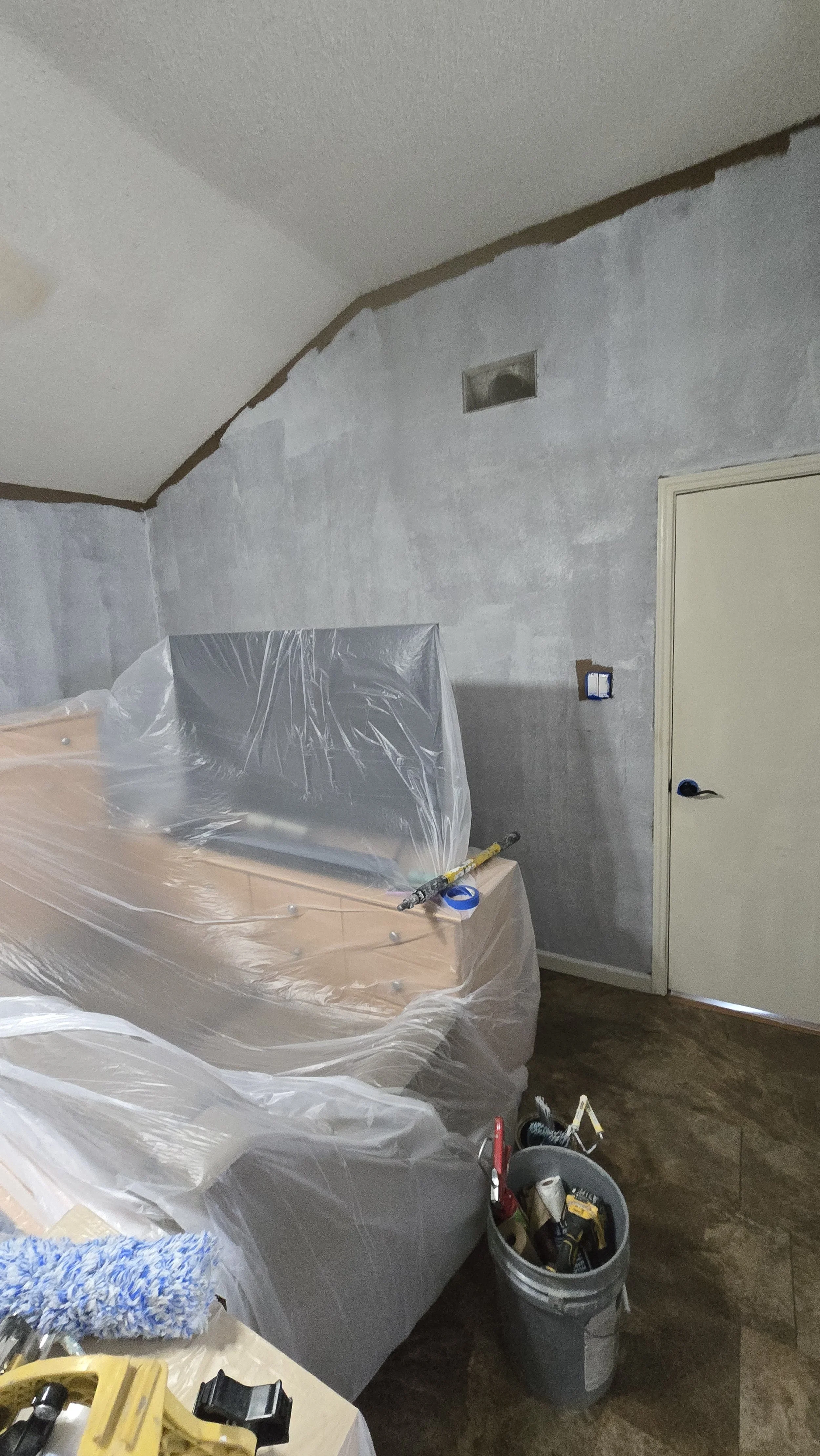 Room under renovation with partially painted walls, covered furniture, and various tools and supplies.