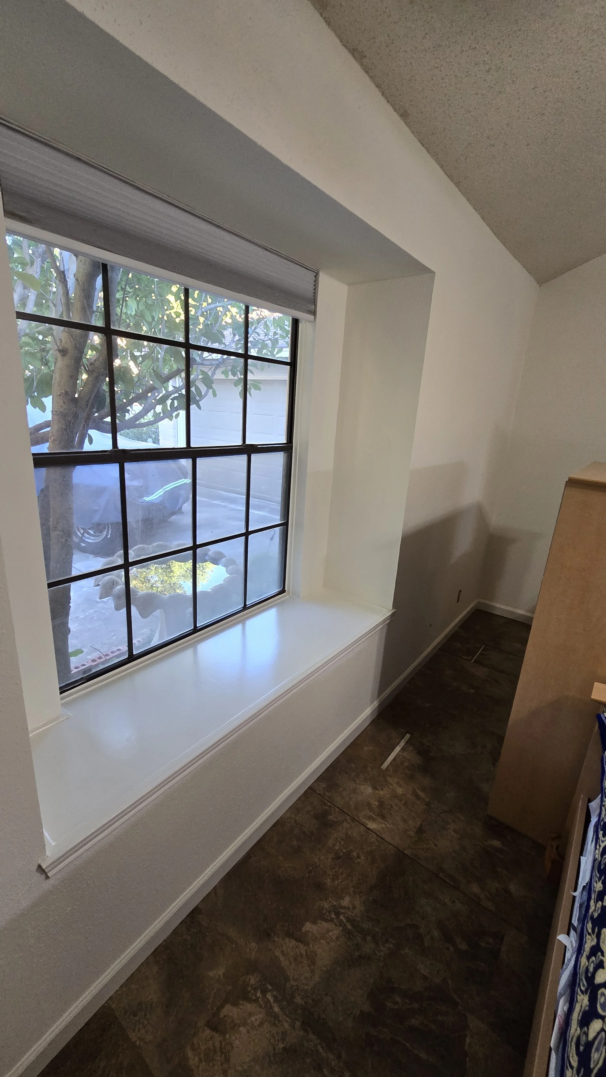 View of a window with a plant outside, a parked car, and a garage, with a windowsill and wood flooring inside a room.