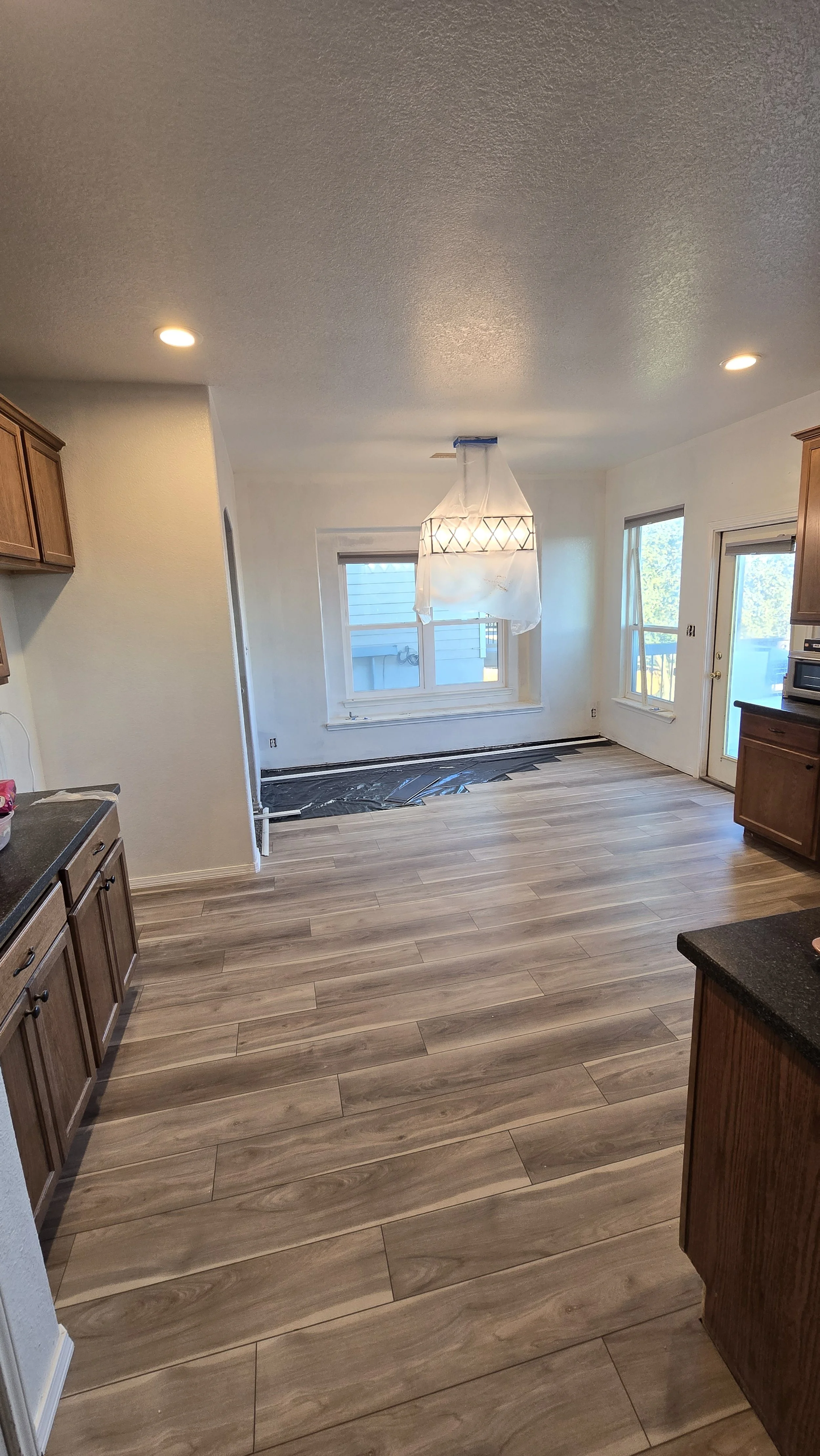 Empty kitchen and dining area with wooden cabinets, hardwood flooring, and natural light from windows.