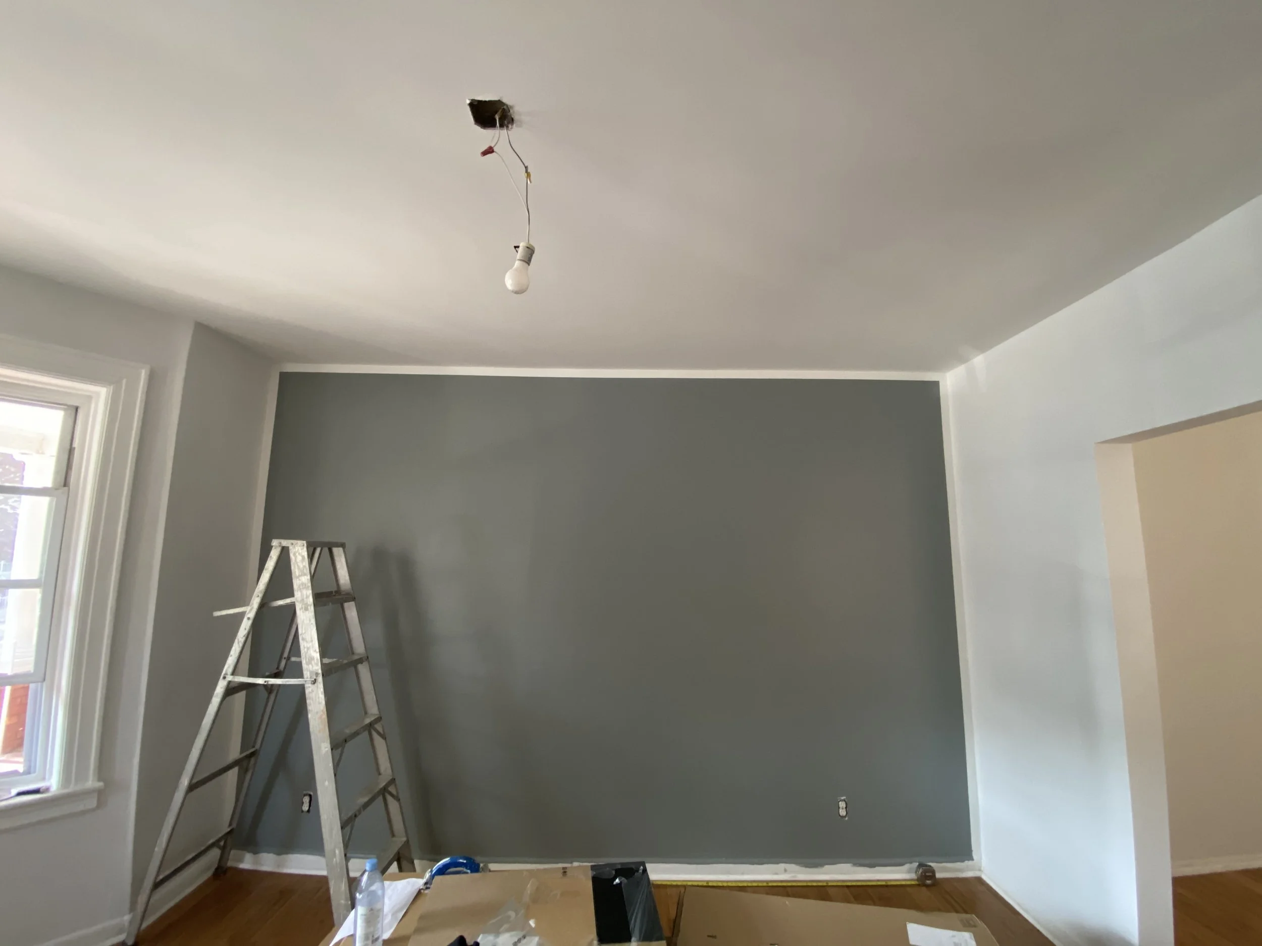 Room undergoing renovation with a gray accent wall, ladder, and construction supplies.
