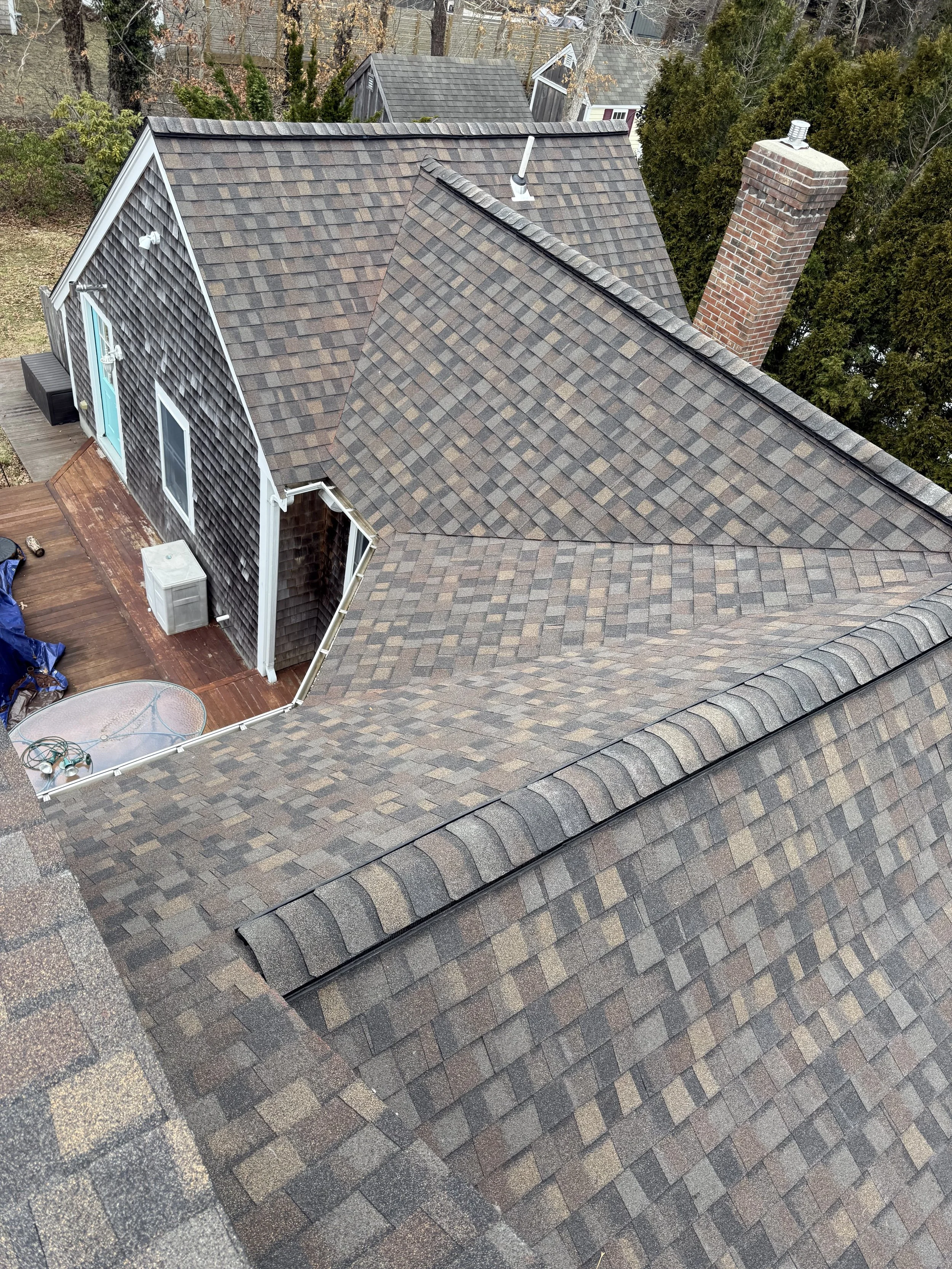 Aerial view of a house roof with multiple sections, chimney, and surrounding trees.