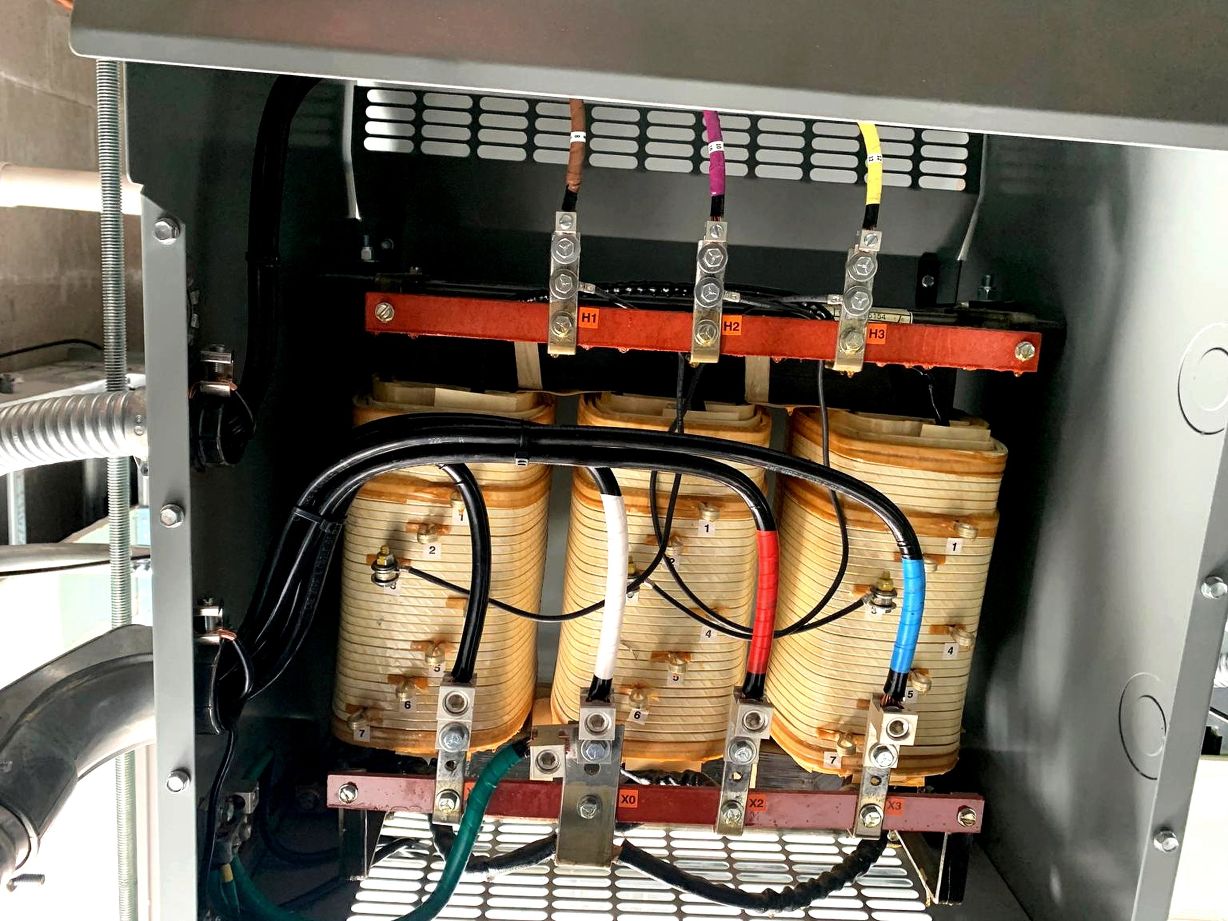 Inside view of an electrical transformer showing coils, wires, and connections.