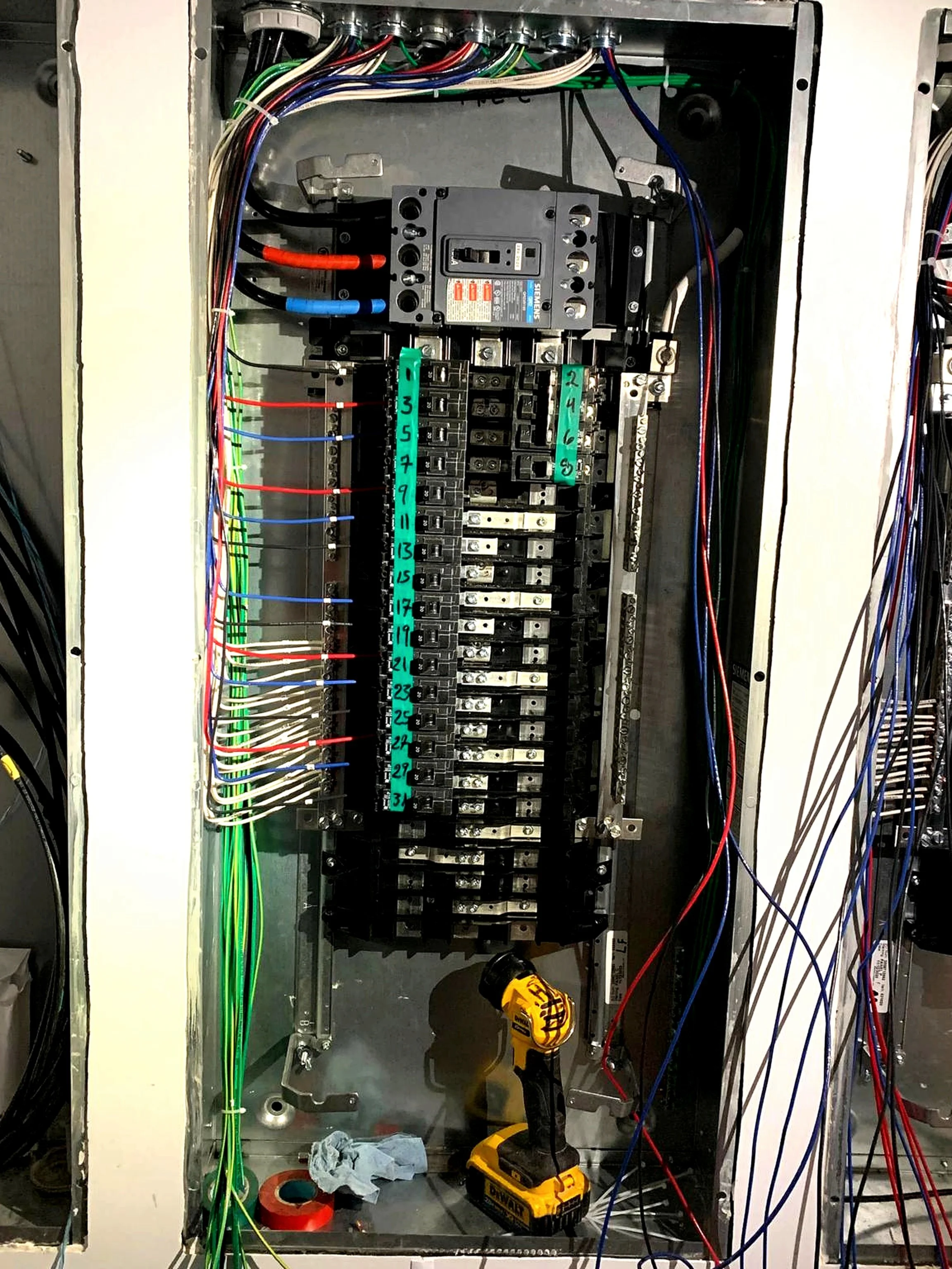 Open electrical panel with wiring, circuit breakers, and tools inside.