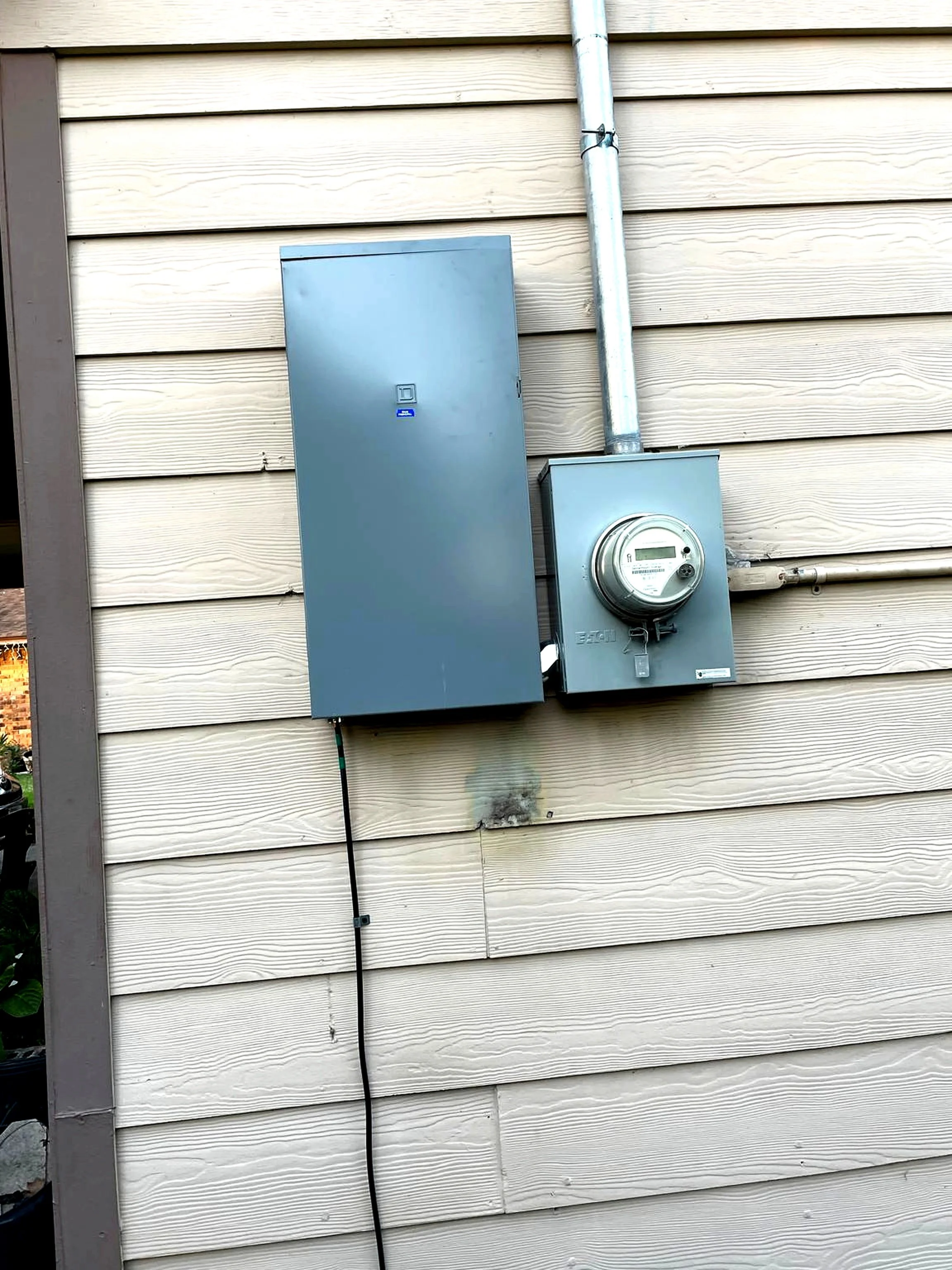 Exterior wall with electrical meter, gray conduit, and black cable attached to a siding wall.