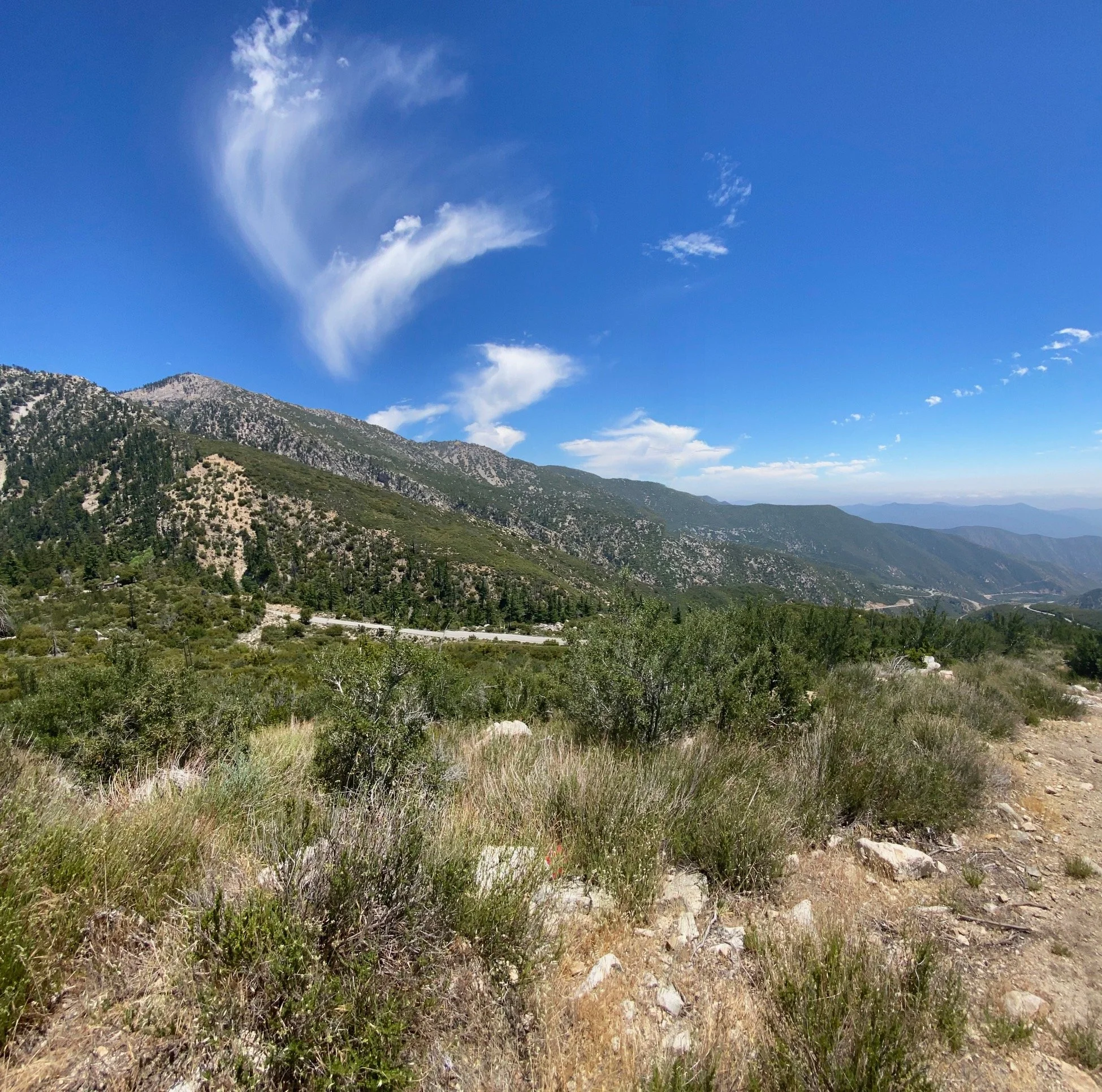 A scenic mountain landscape with a bright blue sky, scattered clouds, and green vegetation on the hillside.
