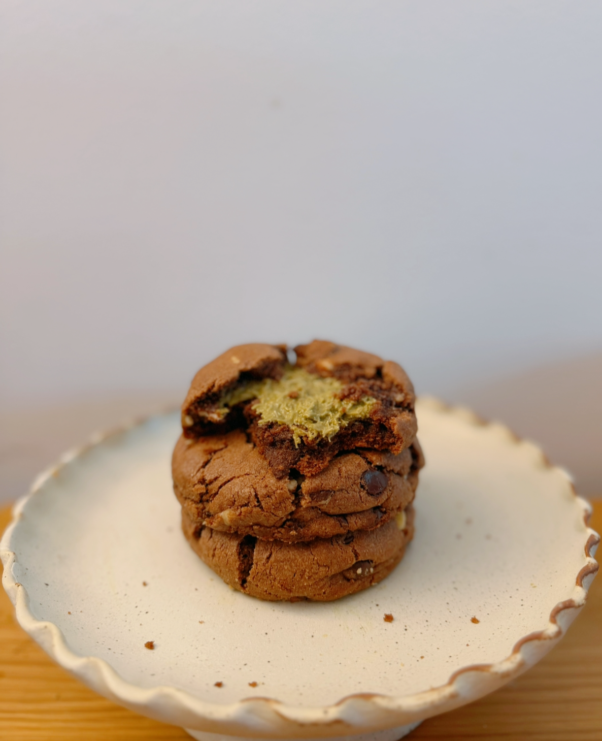 A plate with three stacked chocolate chip cookies, with the top cookie partially bitten, showing green and yellow filling inside.