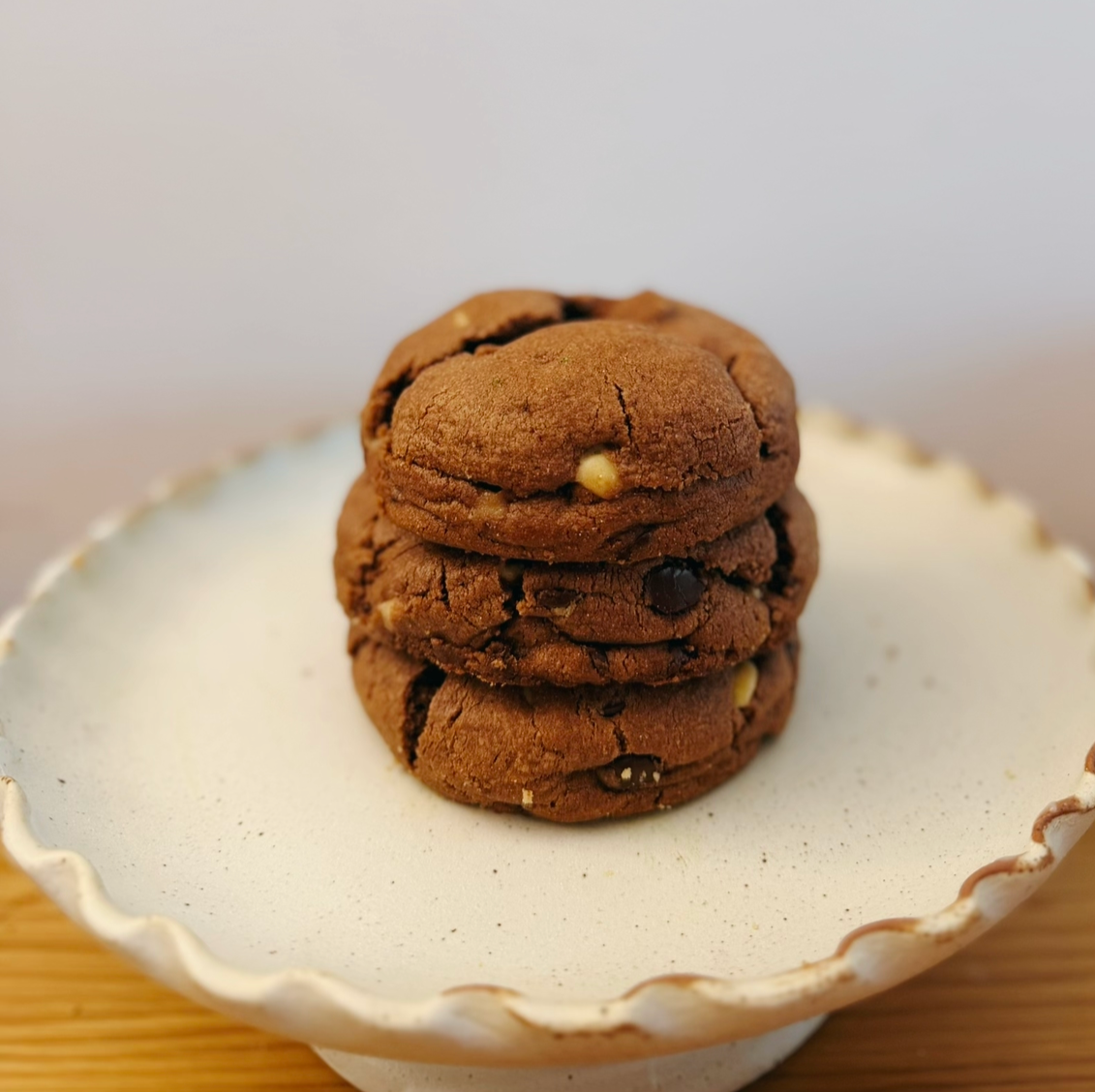 Stack of three chocolate cookies with white and dark chocolate chips on a white, scalloped dish.
