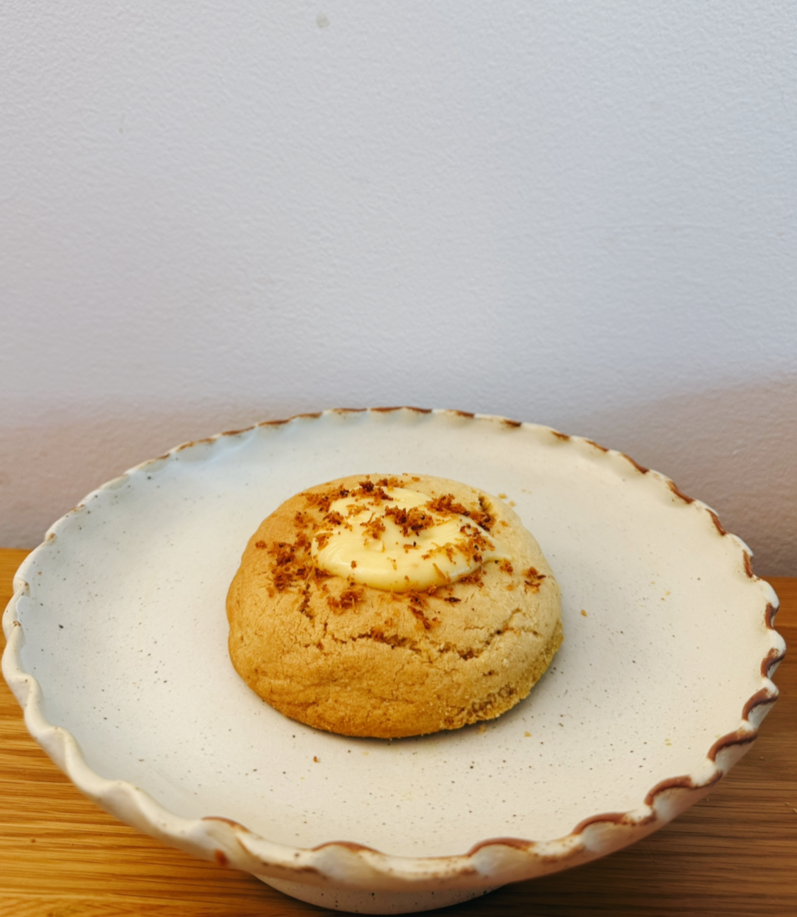 A cookie with a dollop of cream and sprinkled crumbs, on a white scalloped plate.