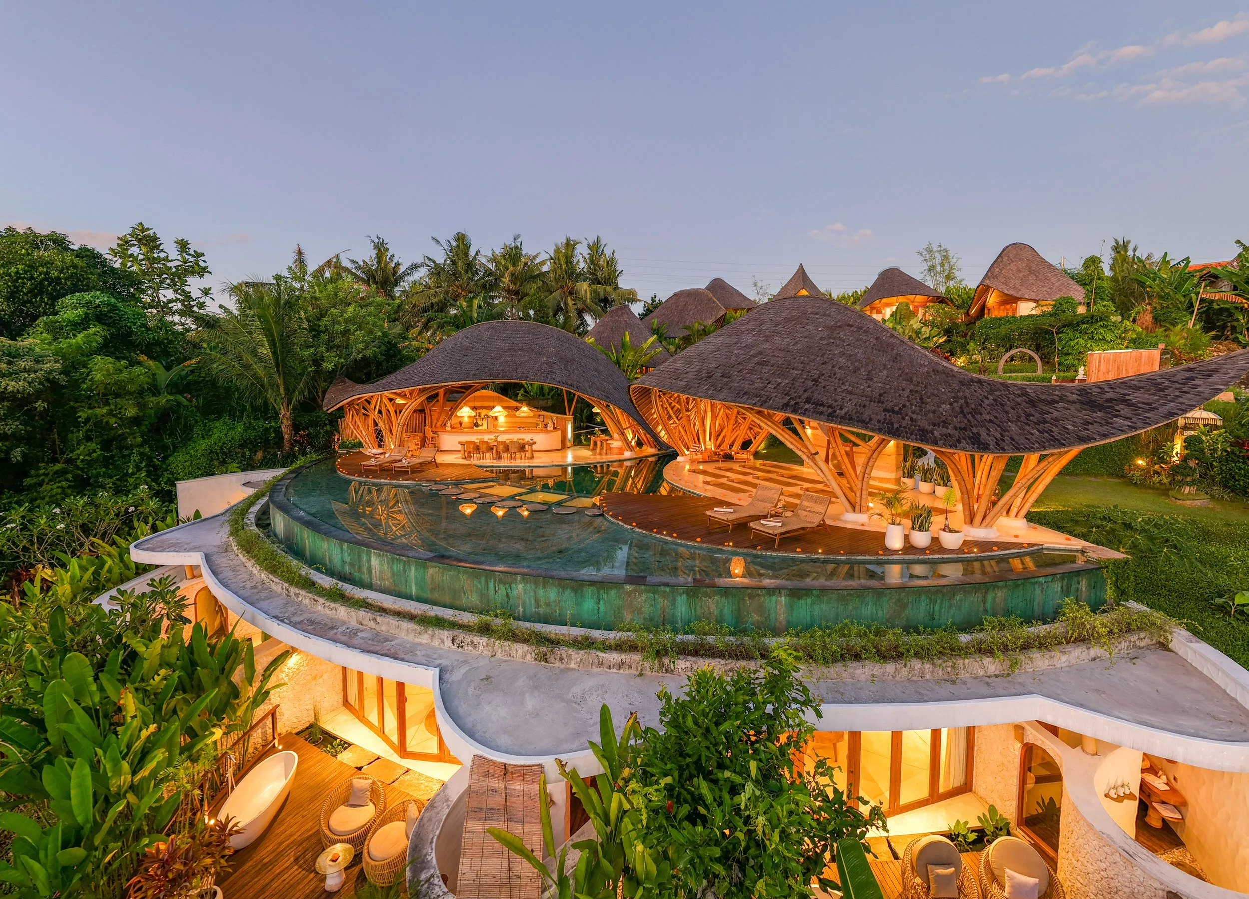 Luxury treehouse resort with curved wooden roofs, outdoor pool, lush tropical greenery, and warm lighting at dusk, overlooking the jungle.