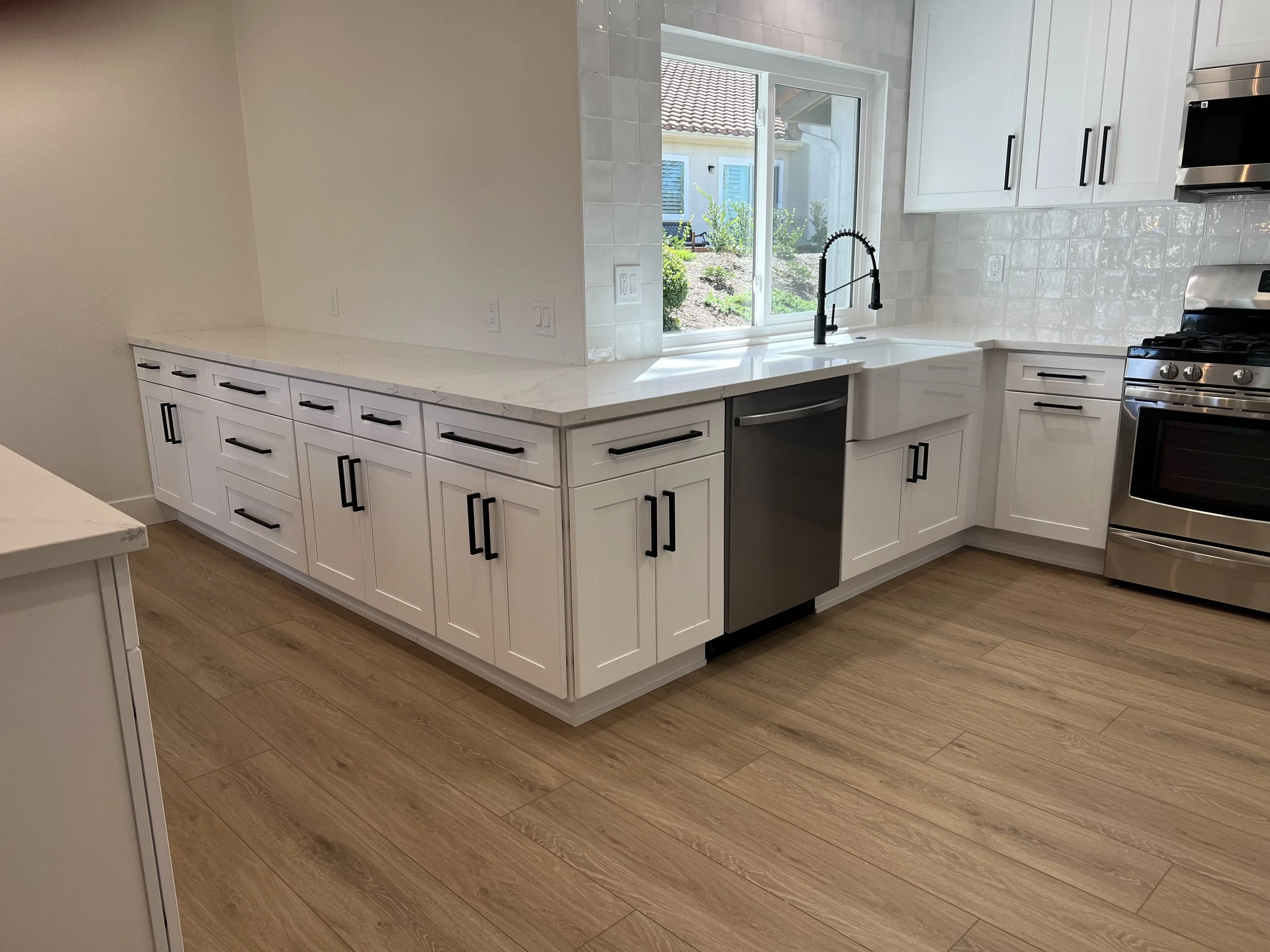 Modern kitchen with white cabinets, a large window, and a stainless steel stove. Light hardwood flooring and a marble countertop.