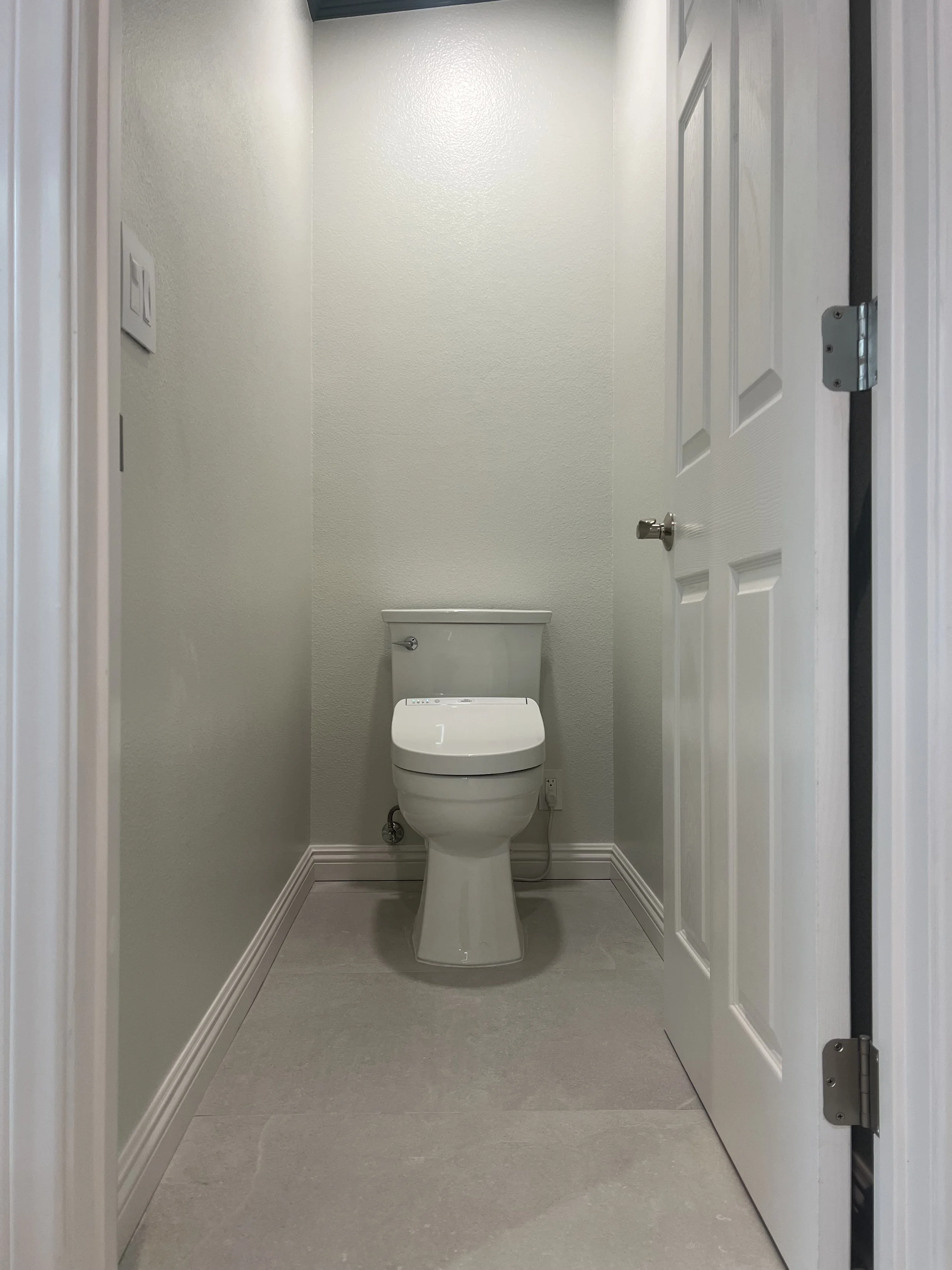 An empty small bathroom with a toilet, light-colored walls, and a closed door.
