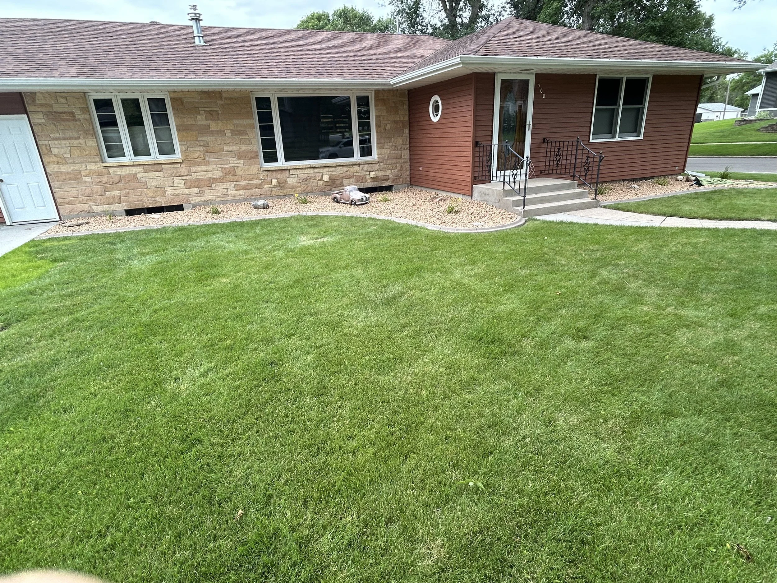 Professional lawn care and landscape edging in Watertown, SD featuring a healthy green lawn and decorative rock bed installation for a clean, low-maintenance finish.