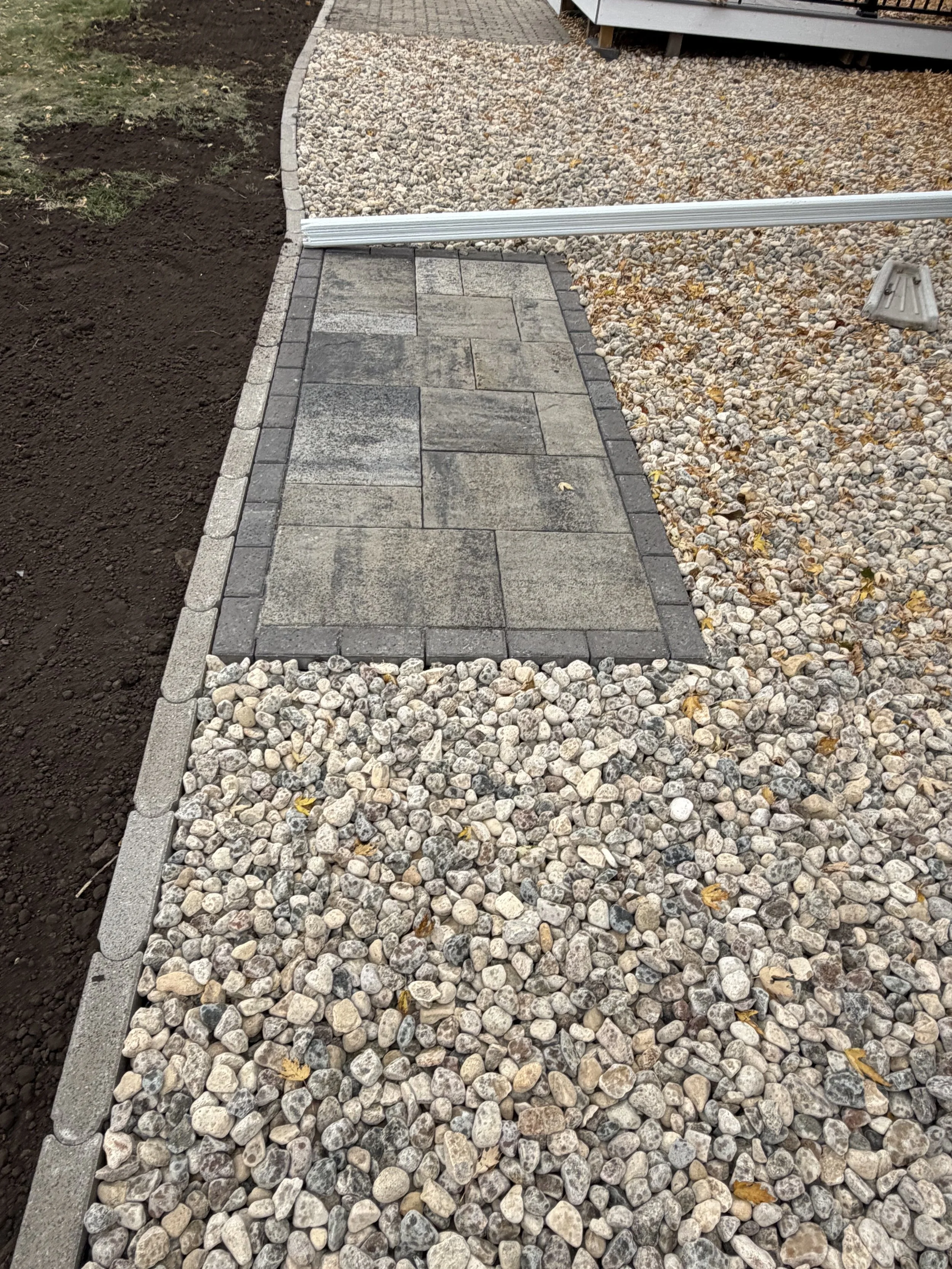 Paver walkway installation in Watertown, SD with decorative rock landscaping and edging, creating a clean, durable, and low-maintenance pathway around the home.