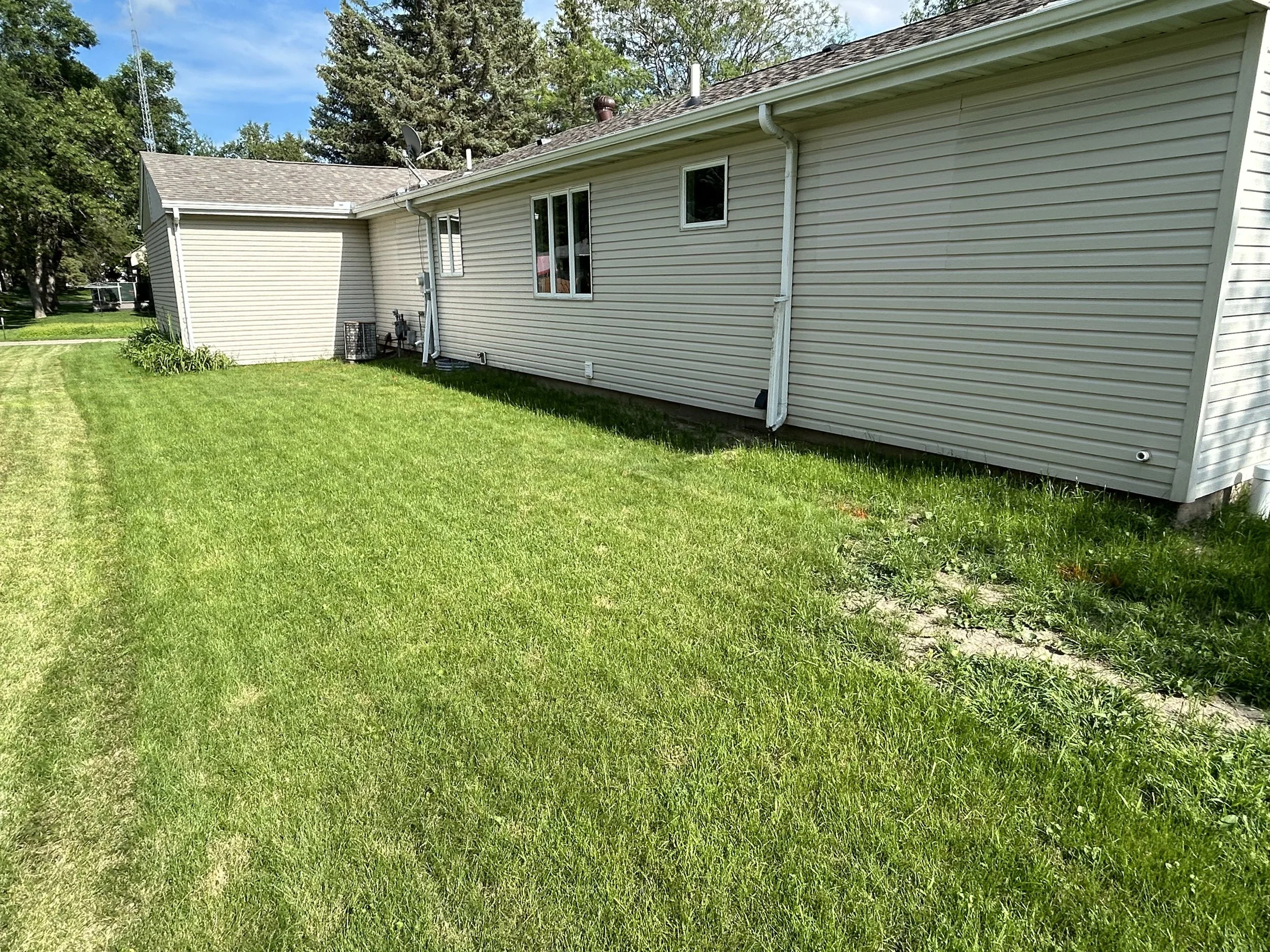 Landscape renovation before photo in Watertown, SD showing overgrown lawn edges and unmaintained areas along the home. This stage highlights the need for cleanup, edging, and landscape improvement.