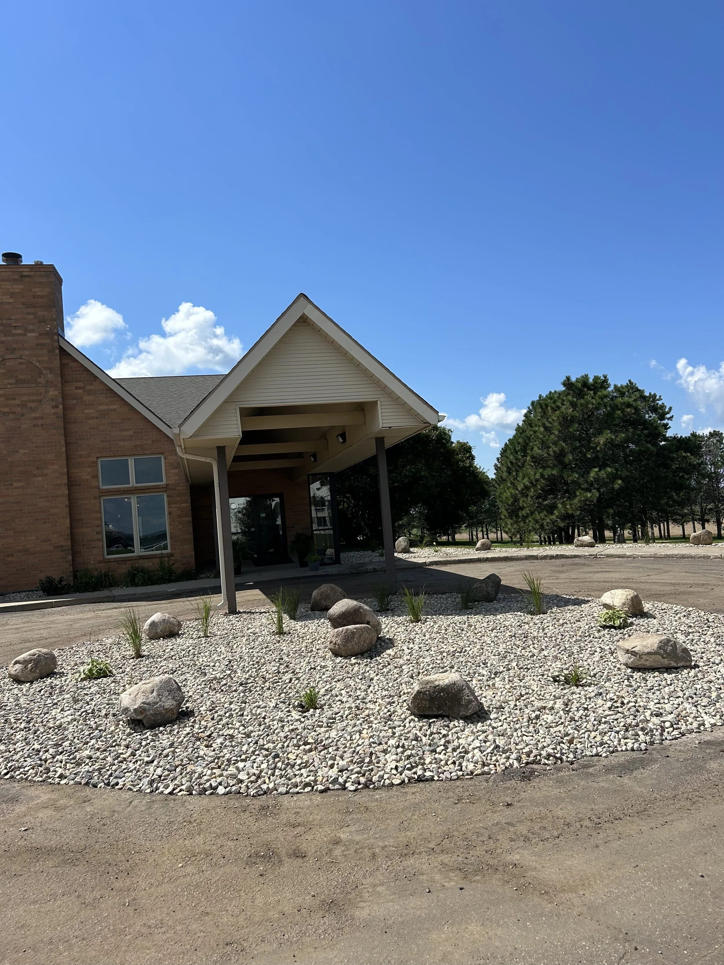 Commercial landscape installation in Watertown, SD featuring decorative rock, boulders, and plantings around a building entrance for a clean, low-maintenance, and professional appearance.
