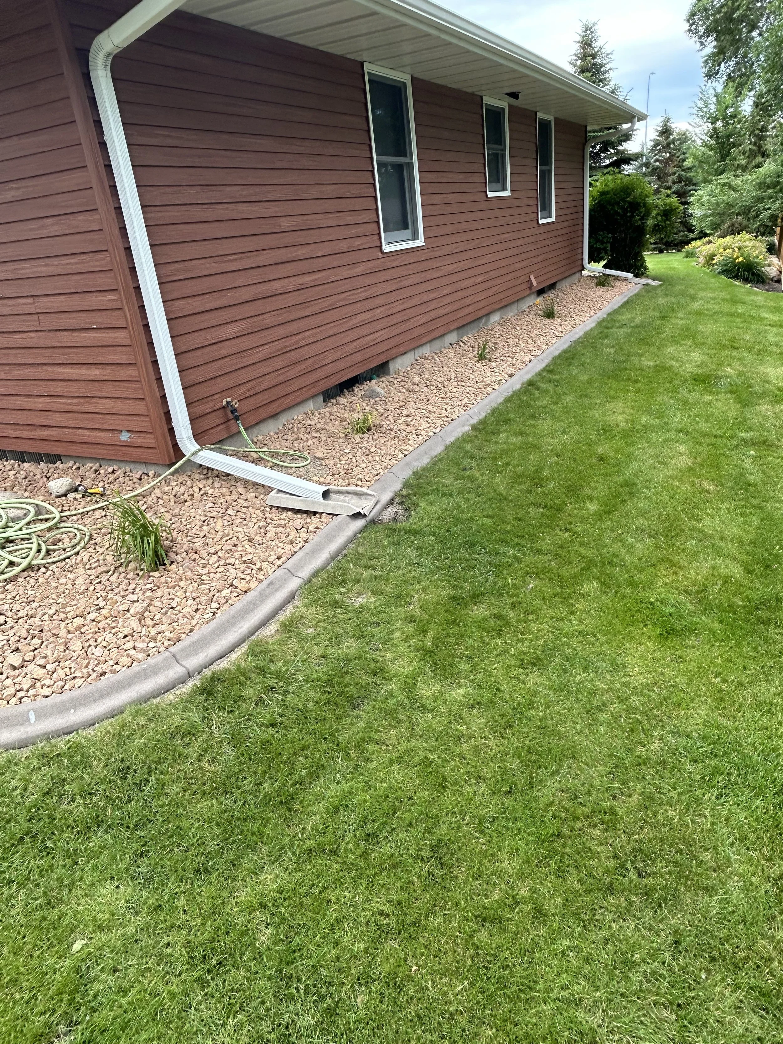 Landscape installation in Watertown, SD with decorative rock, edging, and plantings along a home foundation for improved drainage and curb appeal.