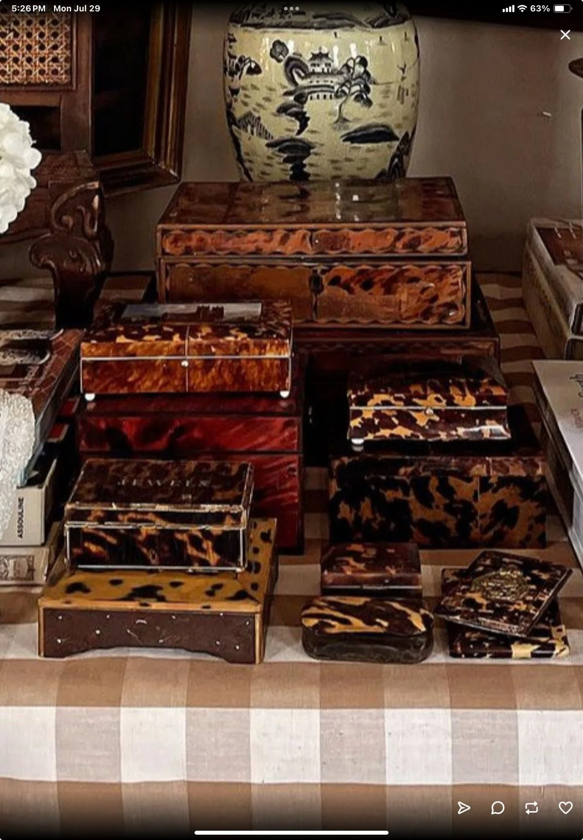 Collection of decorative boxes and trays with animal print patterns, arranged on a checkered tablecloth in a room with a large porcelain vase and wooden furniture.