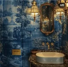 Bathroom with blue wallpaper, gold wall sconce, mirror, and sink with marble countertop.