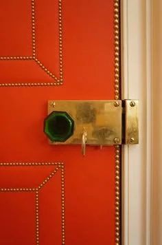 Close-up of a red door with brass hardware, including a green octagonal peephole and a door latch.