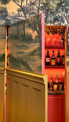 A vintage-style bar with a painted landscape on the exterior, partially open to reveal bottles of alcohol and glassware inside, with trees and sky visible in the background.