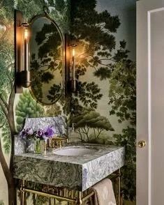 Bathroom with a marble sink, oval mirror, black wall-mounted light fixtures, and a nature-themed wallpaper with trees and foliage.