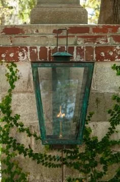 A vintage green lantern with a candle inside, hanging on a brick and stone wall with greenery in the background.