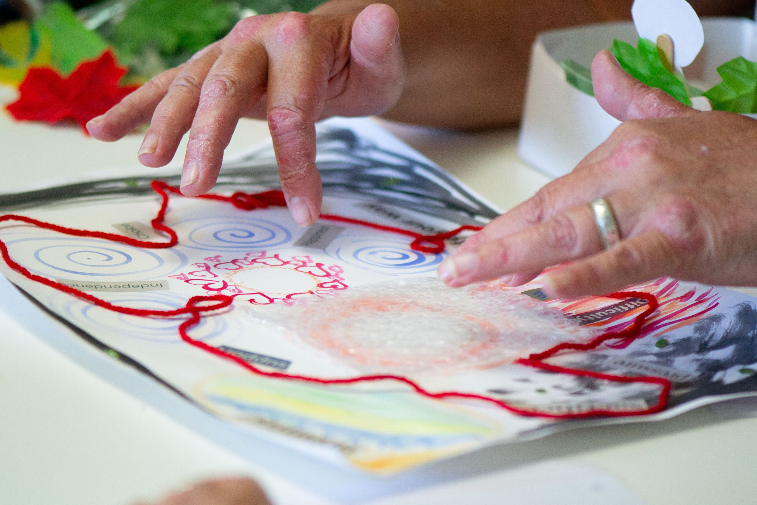 Close-up of hands working on a craft project with papers, yarn, and decorative items on the table.