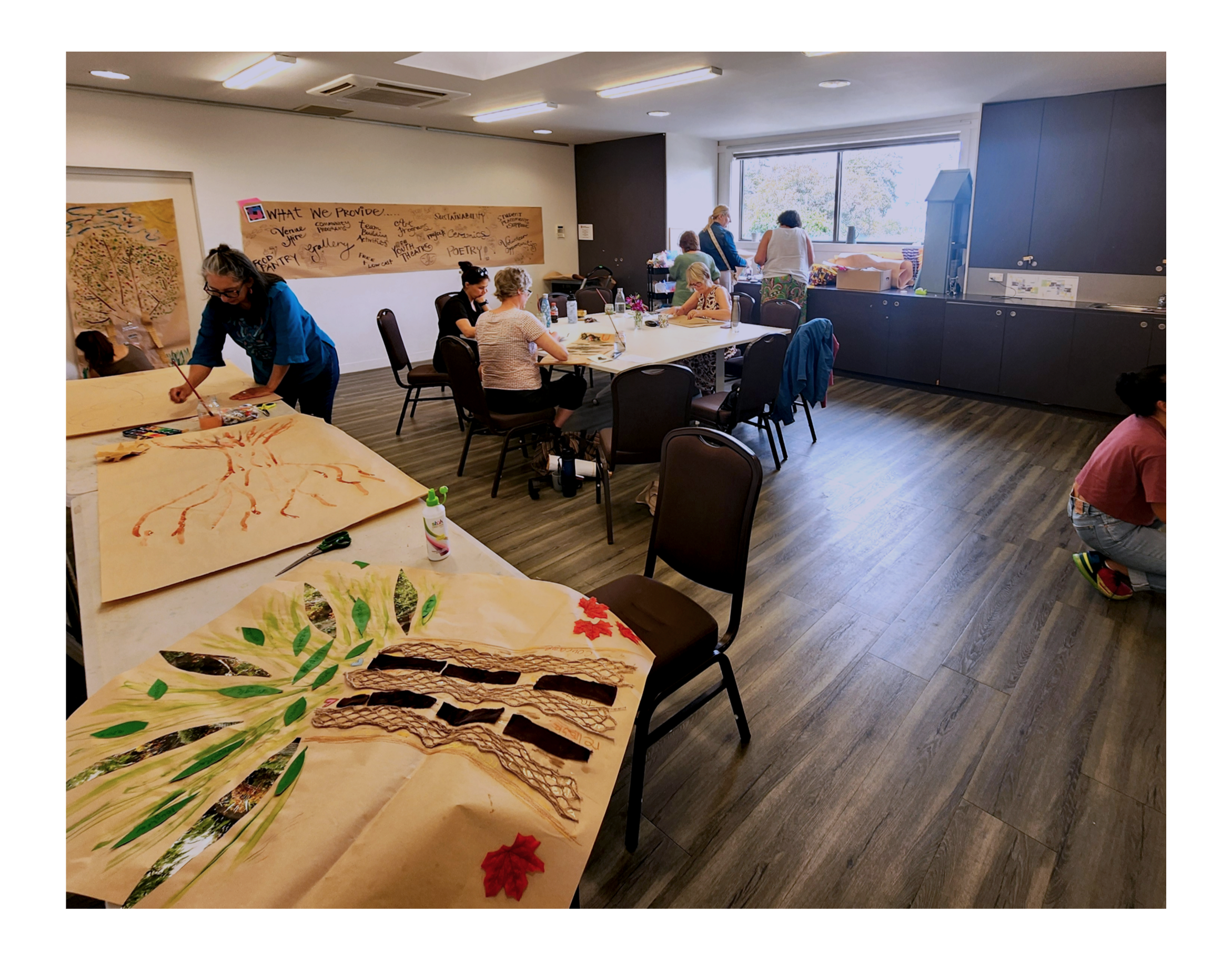 People participating in an arts and crafts workshop, creating and displaying nature-themed artwork in a well-lit room with large windows.