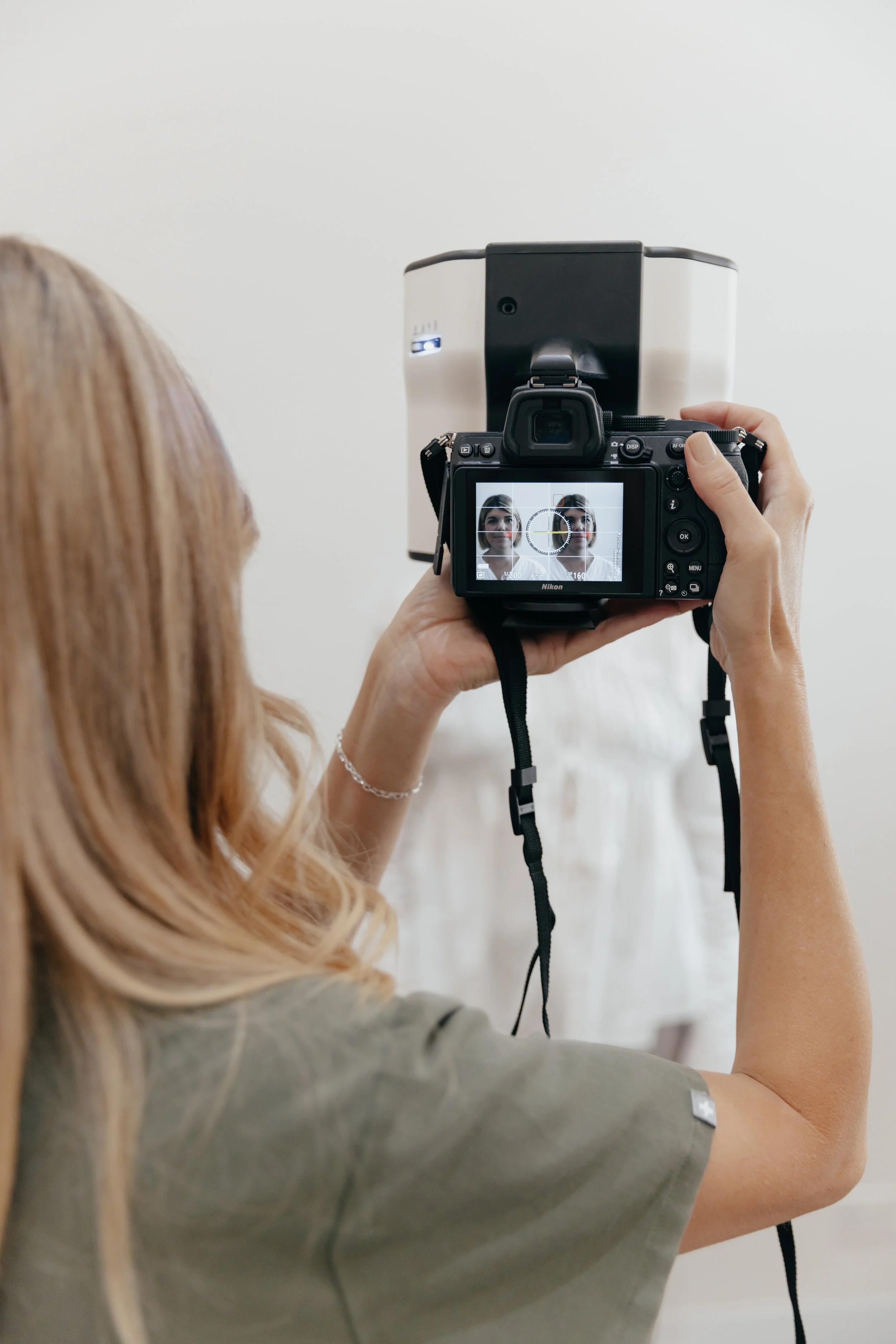 A woman taking a photograph of a white dress with a camera, which is displayed on a camera screen with a focus grid.