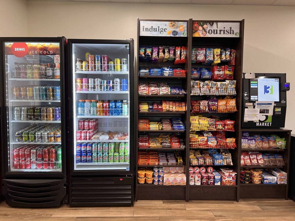 Grocery store snacks and drinks section with refrigerated drinks and snack shelves labeled 'Indulge' and 'Nourish'.