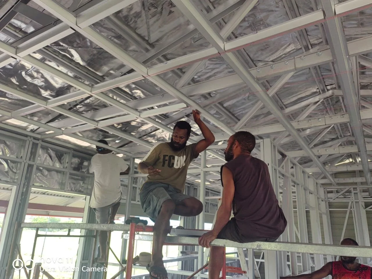 Three construction workers inside a building framework, assembling the metal roof structure.