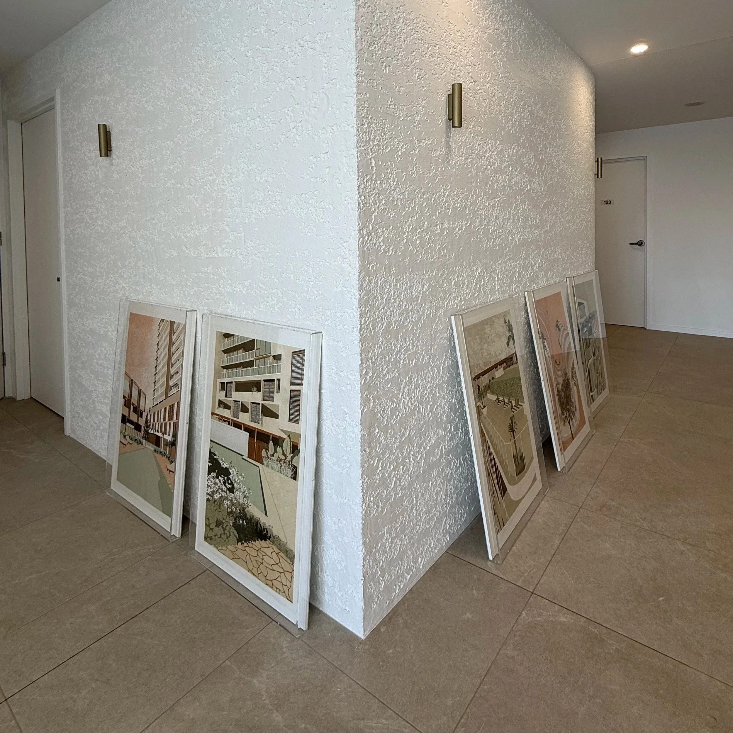 Display of framed architectural drawings or blueprints on a white textured wall in an indoor setting.