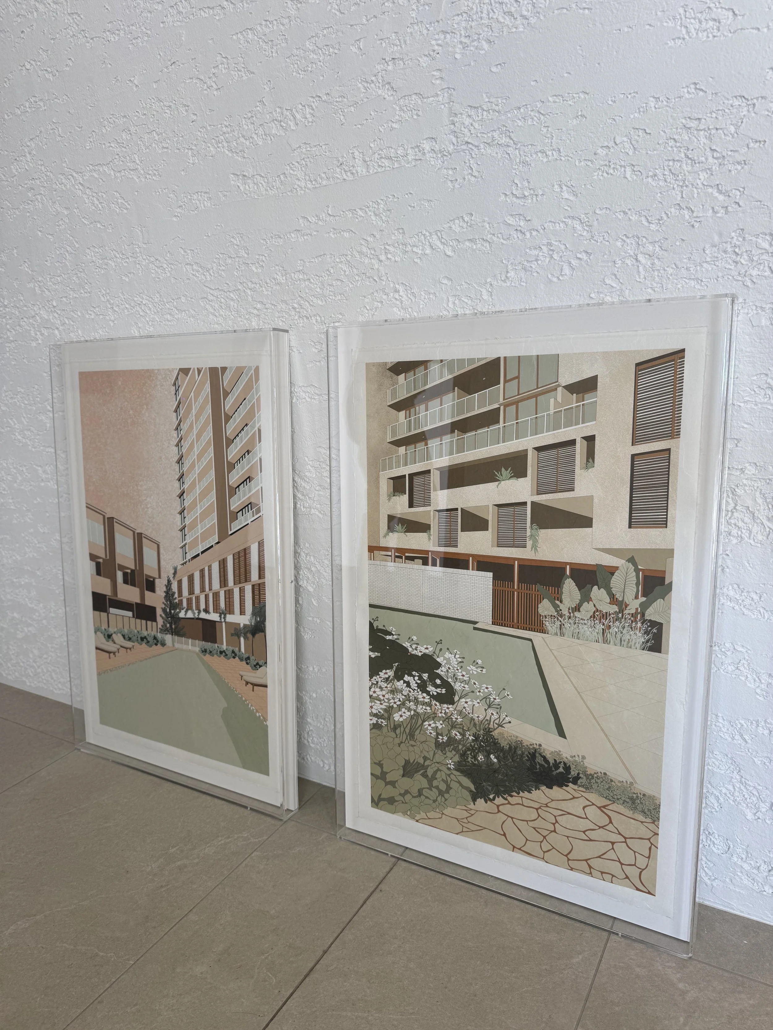 Two architectural renderings displayed on transparent panels, showing modern residential buildings with balconies, large windows, and landscaped outdoor areas.
