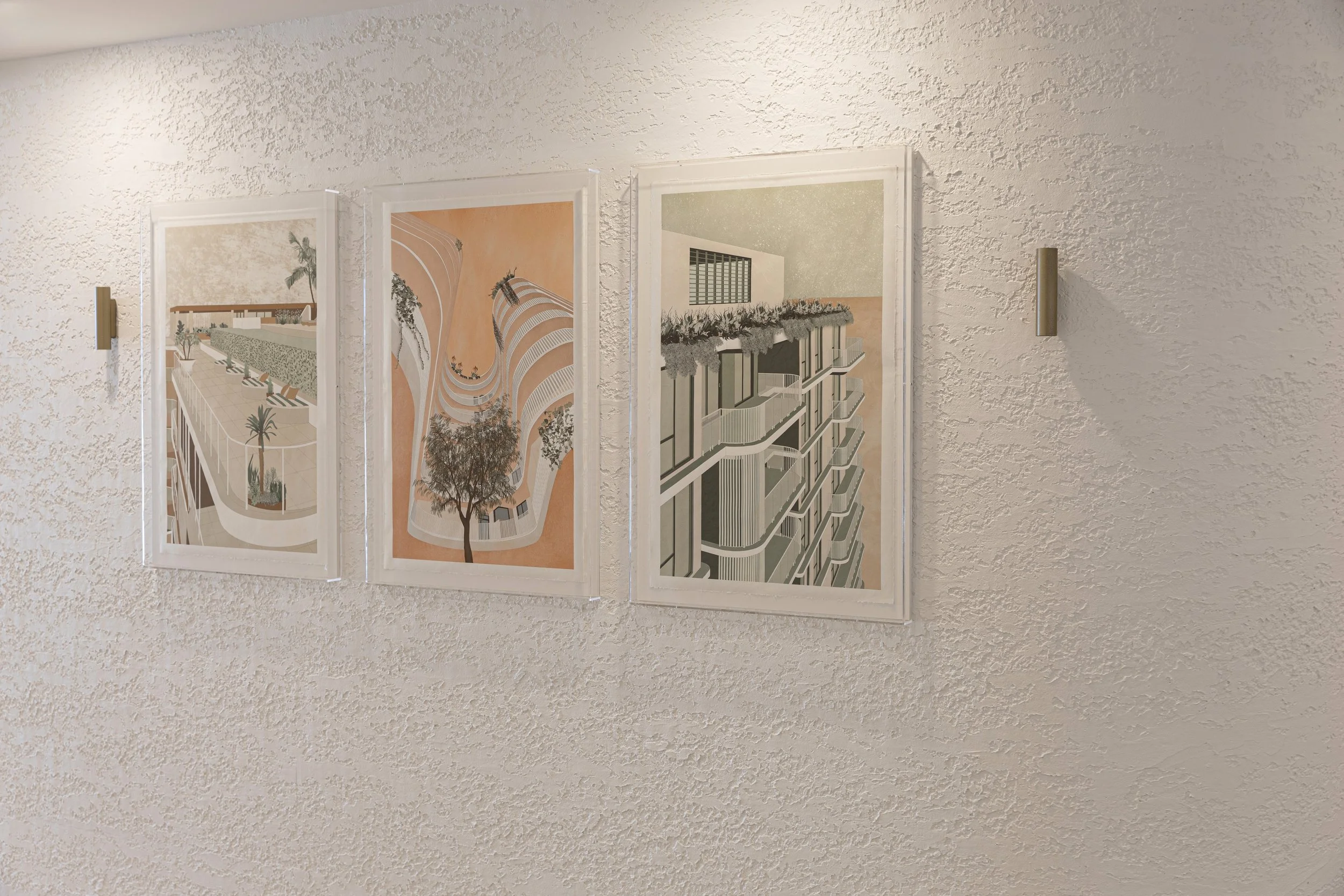 Three architectural drawings framed and mounted on a textured white wall.