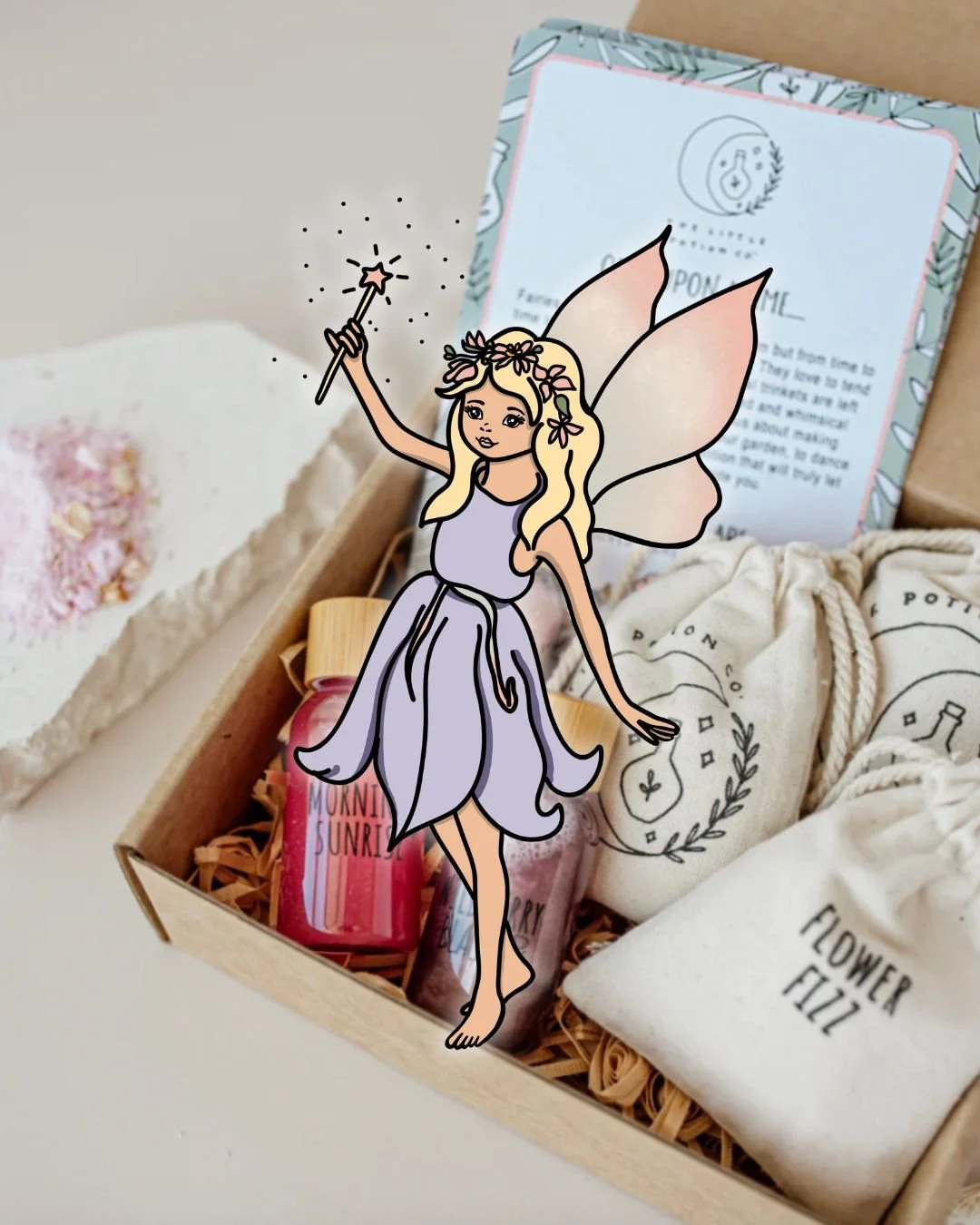 Illustration of a fairy with blonde hair, pink wings, and a lavender dress holding a magic wand, superimposed over a gift box containing bath products.