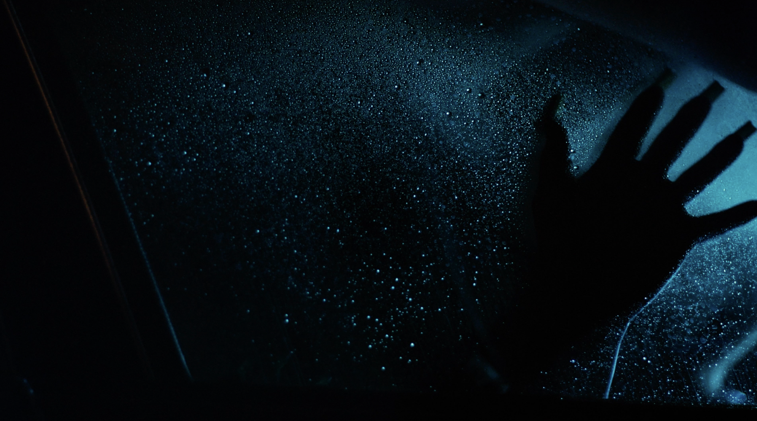 Silhouette of a hand reaching out towards a glowing blue surface with scattered light particles, creating a cosmic or space-like effect.