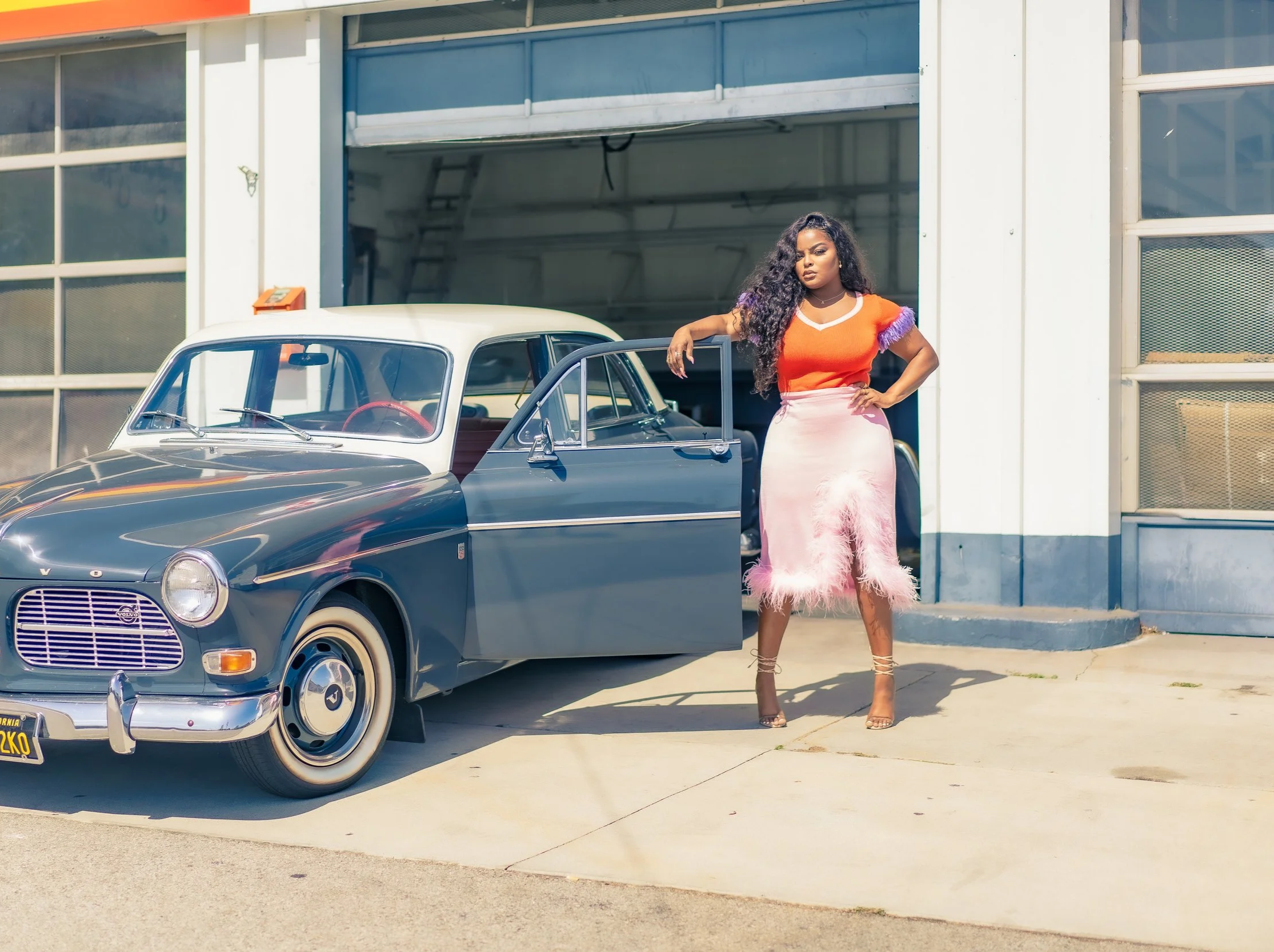 A woman standing beside a vintage black and white car outside a garage.