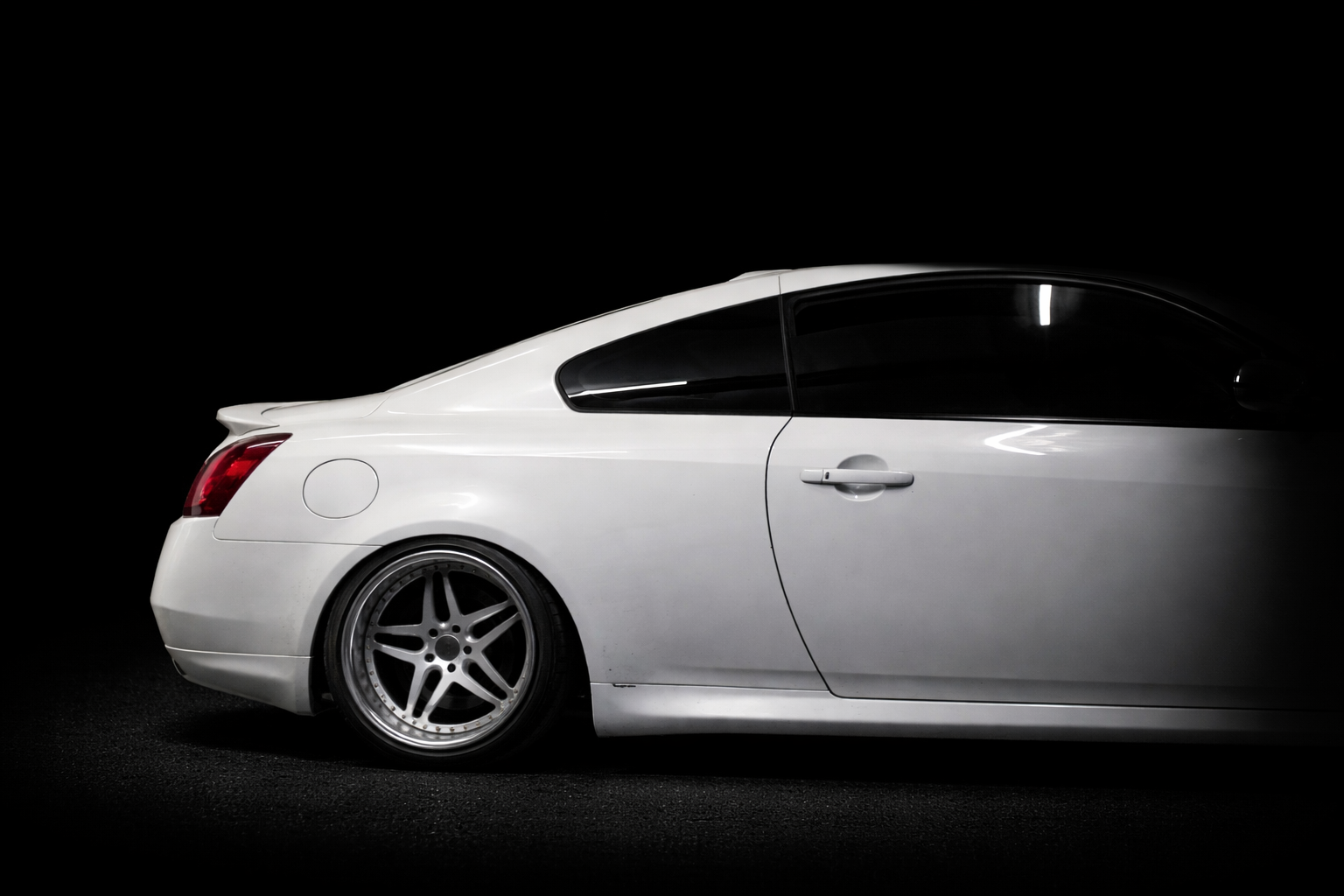 Side view of a white sports car with tinted windows, black tires, and dark background.